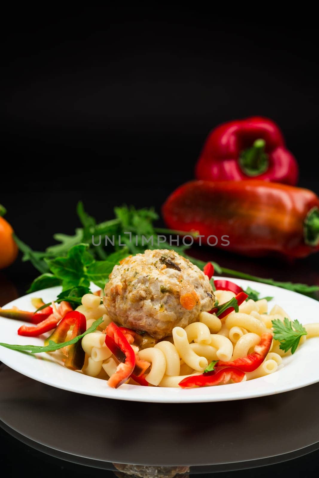 cooked pasta with meatballs, peppers and herbs with spices in a plate, isolated on a black background