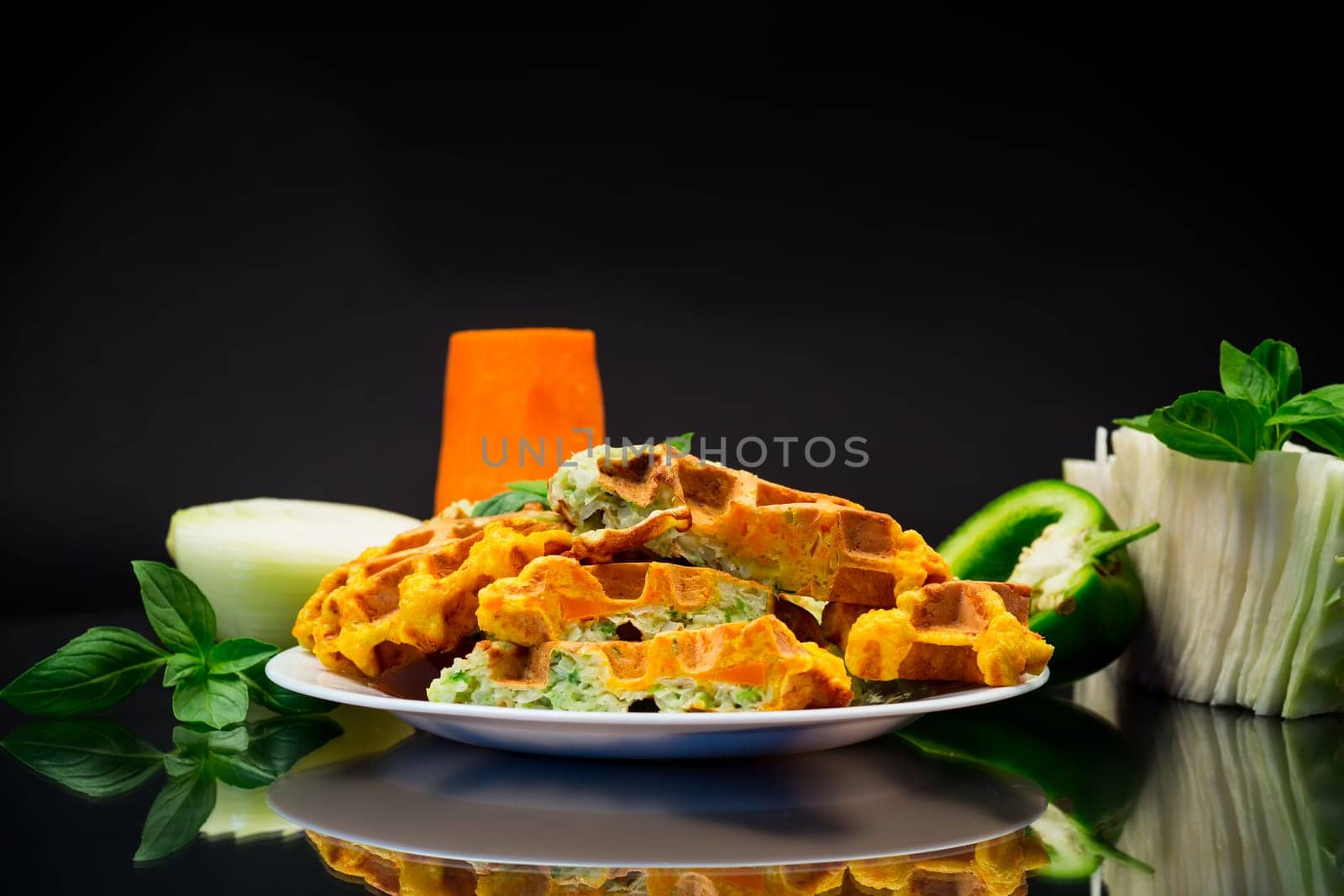 cooked two-color vegetable waffles made from cabbage and carrots, in a plate isolated on black background