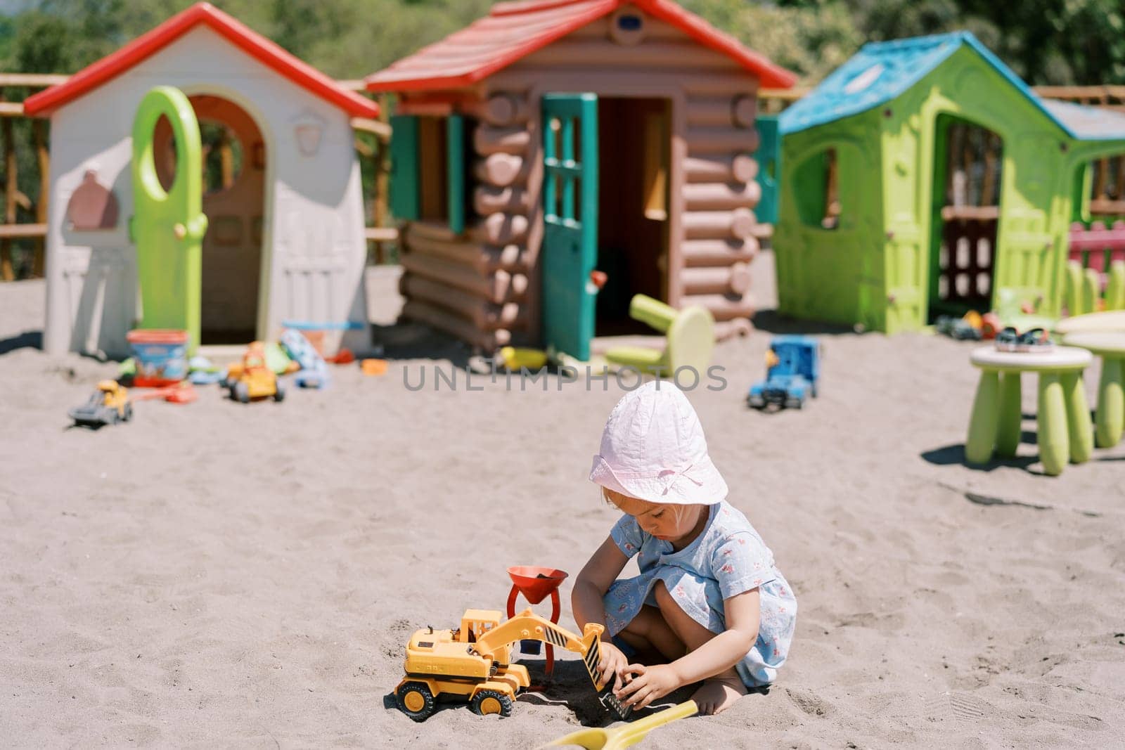 Little girl digs sand with a toy excavator while squatting. High quality photo