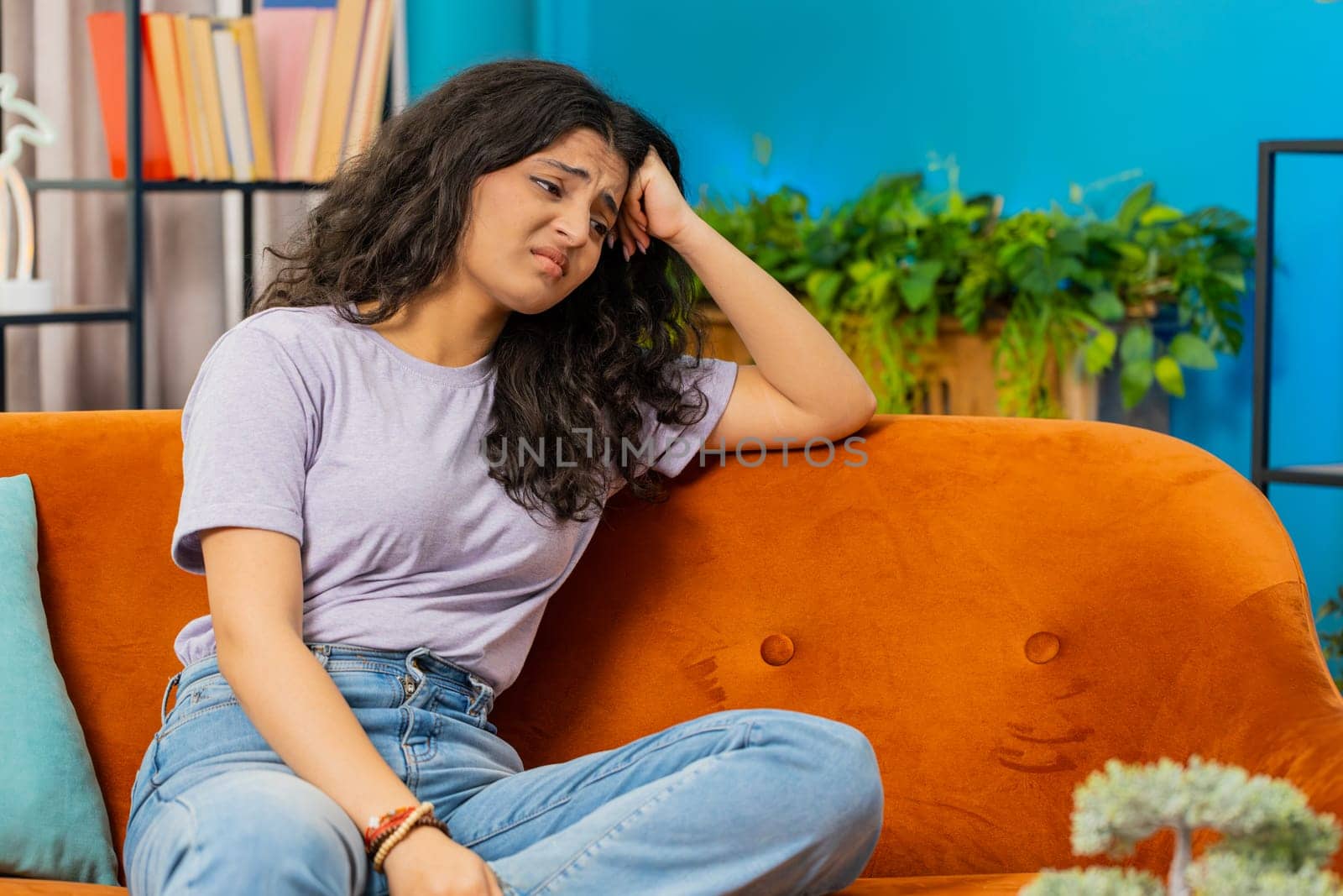Portrait of sad Indian woman girl sitting at home looks pensive thinks over life concerns or unrequited love, suffers from unfair situation. Problem, break up, depressed feeling bad annoyed, burnout