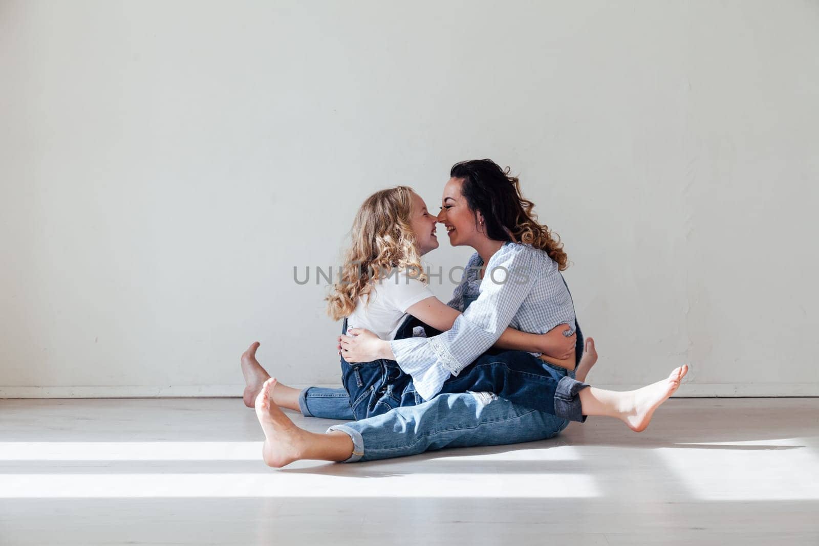 Mom and daughter in denim play in white family love room by Simakov