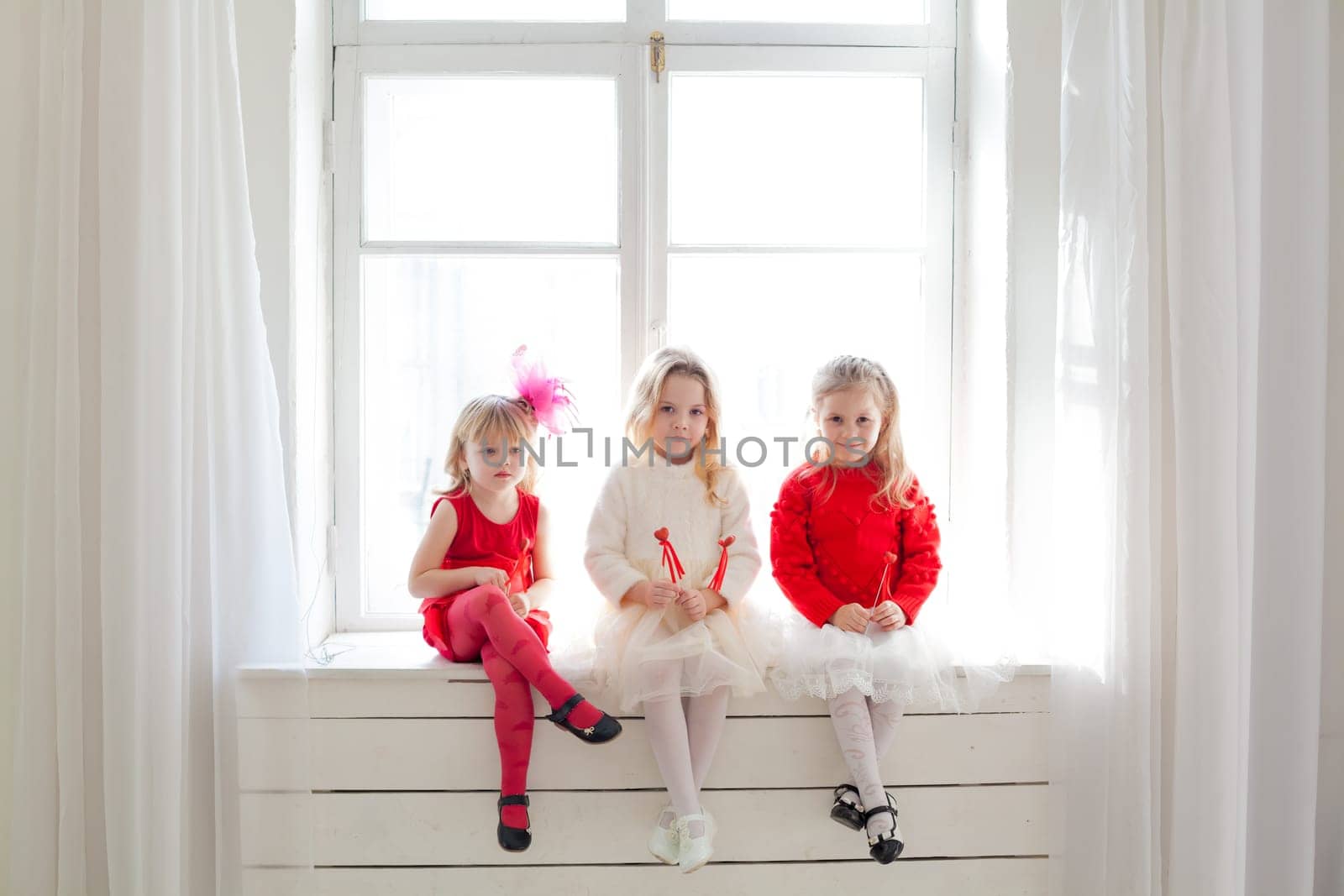 three little girl girlfriends in red and white dresses by the window