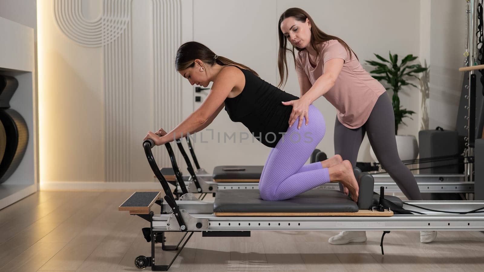 A pregnant woman works out on a reformer exercise machine with a personal trainer