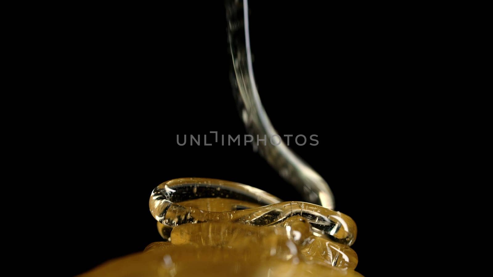Honey sweet flower stream pouring on black background. Golden liquid nectar flows. Thick sweet drops macro view. Healthy syrup, delicious food. High quality