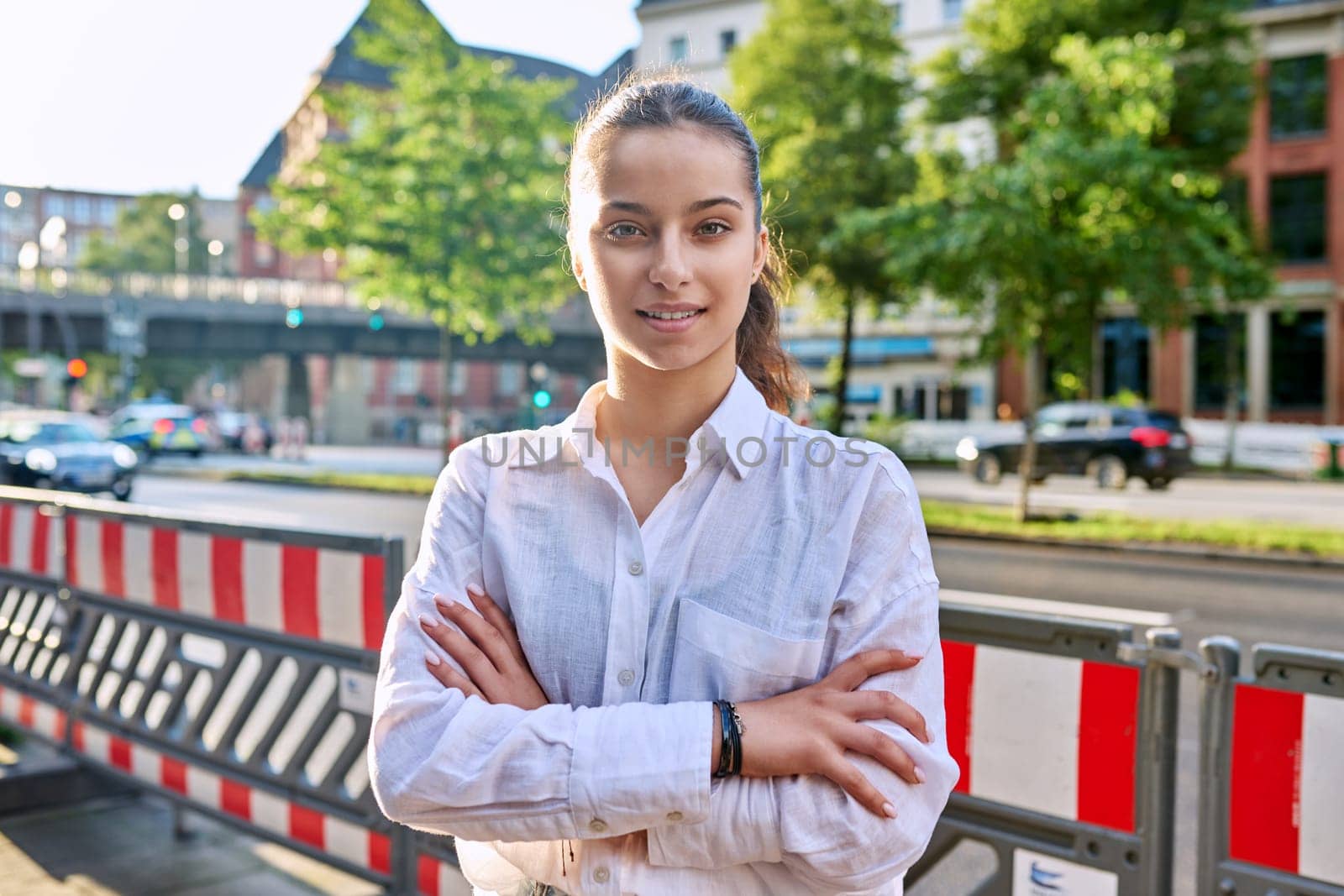Portrait of teenage high school student, smiling confident girl 16, 17 years old looking at camera outdoor, on street of modern city. Urban life, adolescence, education, youth concept