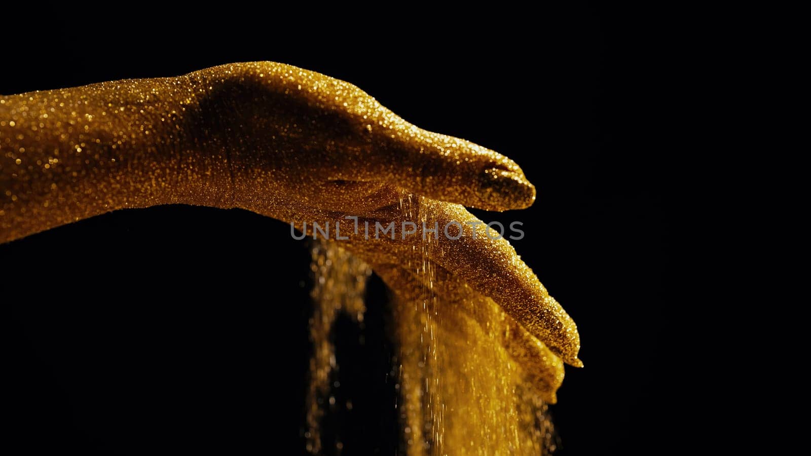 Golden glittering woman hands with dust or sand on black background. Shimmer, time, life moments, deadline, business management, educational creative content concept.