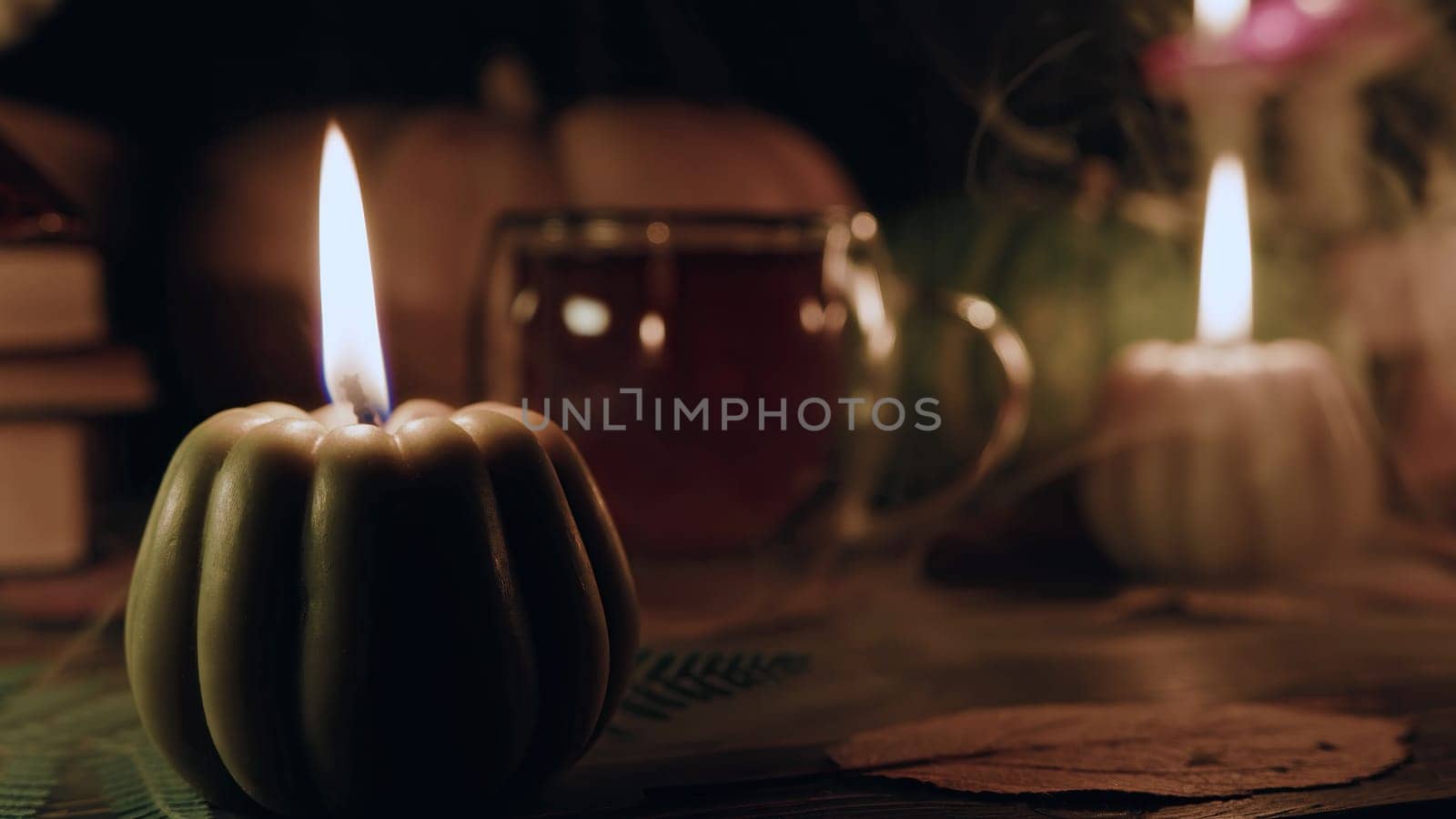 Autumn background. Pumpkin candle, orange fallen leaves. Copy space. Flat lay. Cozy ambiance of fall, candle burning. Seasonal promotions or tranquil visual storytelling.