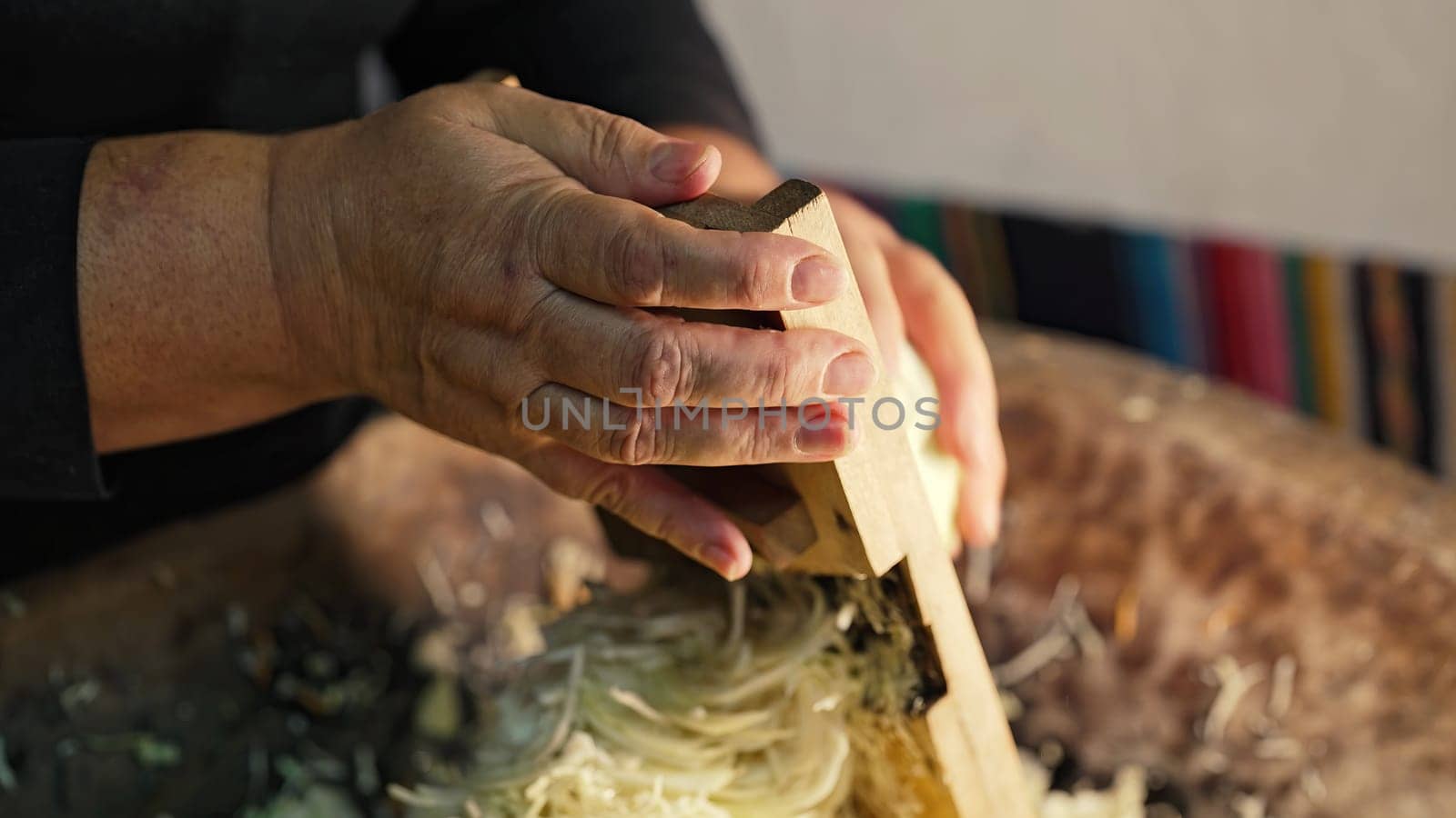 Woman rubs cabbage on grater, cooking traditional ukrainian fermented - sauerkraut salad from shredded carrot. Mixes chopped vegetables in family's ancient wooden trough. High quality