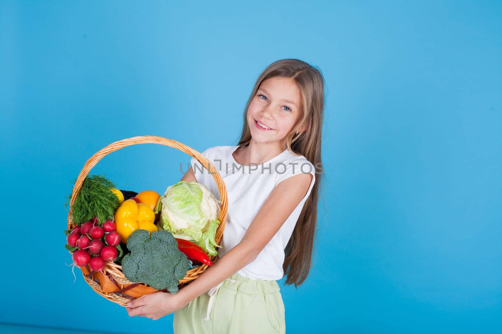 Little girl holds a basket of ripe vegetables radish pepper broccoli