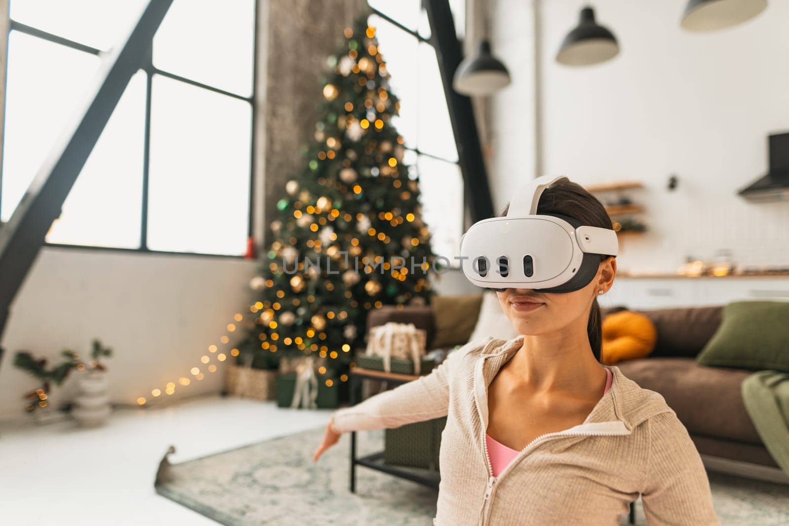 A fitness-oriented young woman practices yoga poses while wearing VR glasses by a Christmas tree. High quality photo