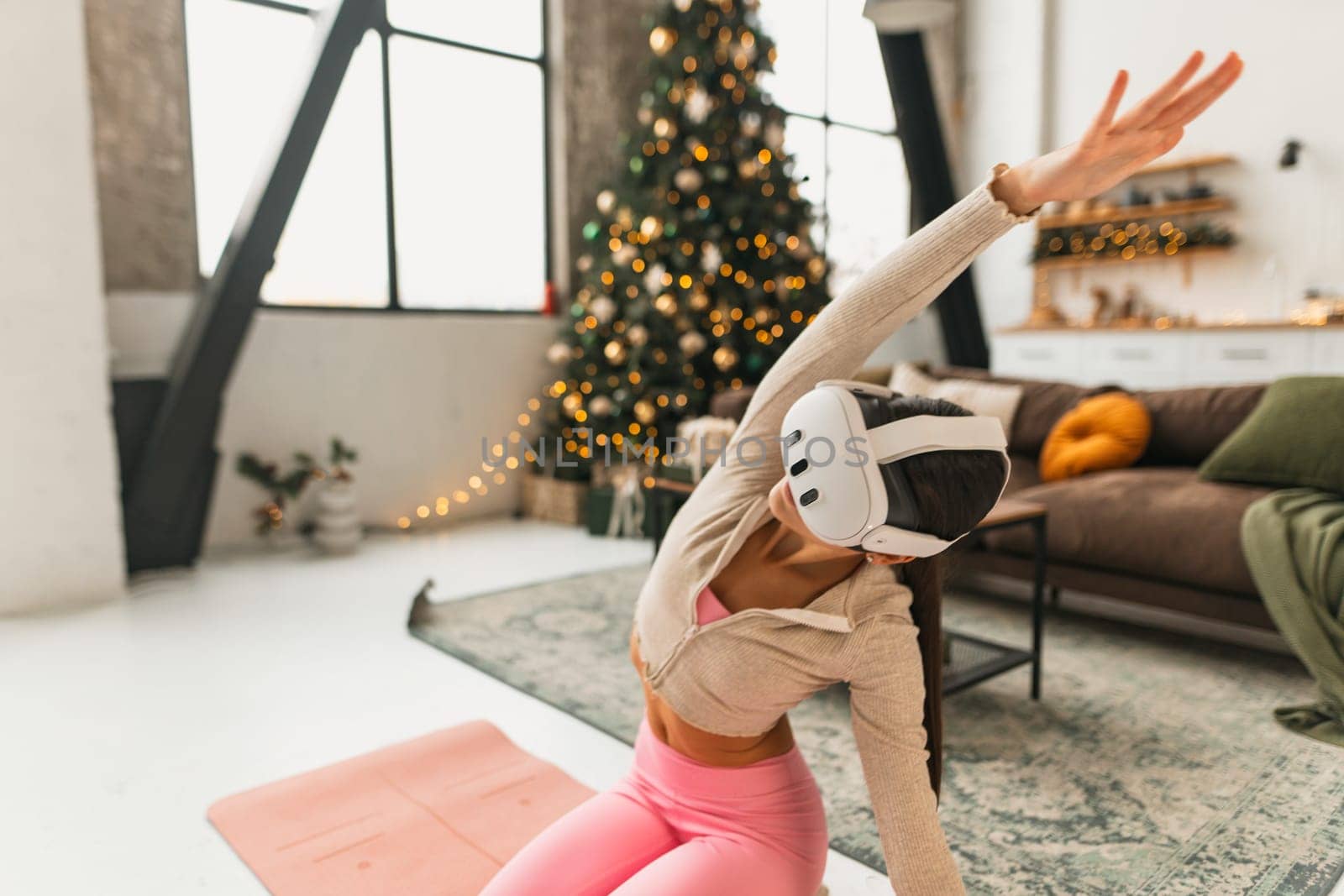 Engaging in yoga poses, a sporty young lady wears VR glasses beside a Christmas tree. High quality photo