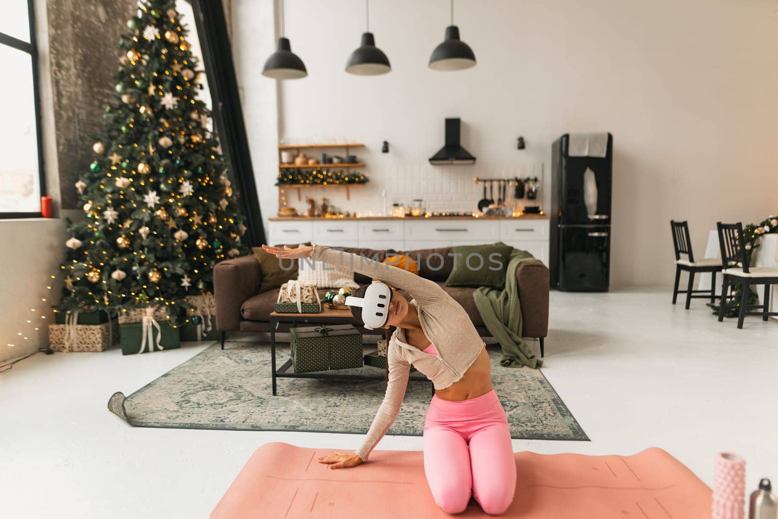 Engrossed in yoga practice, a fitness enthusiast wears virtual reality goggles by a Christmas tree. by teksomolika