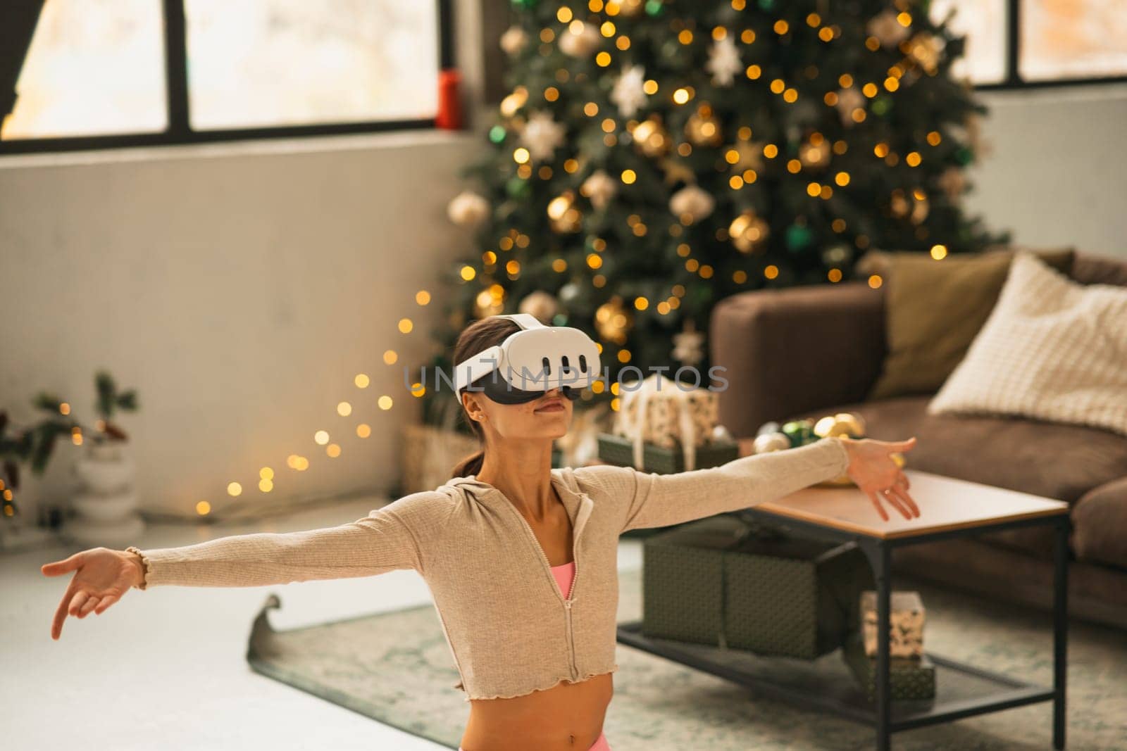 A sporty, fashionable woman wearing a virtual reality headset engages in yoga poses next to a Christmas tree. High quality photo