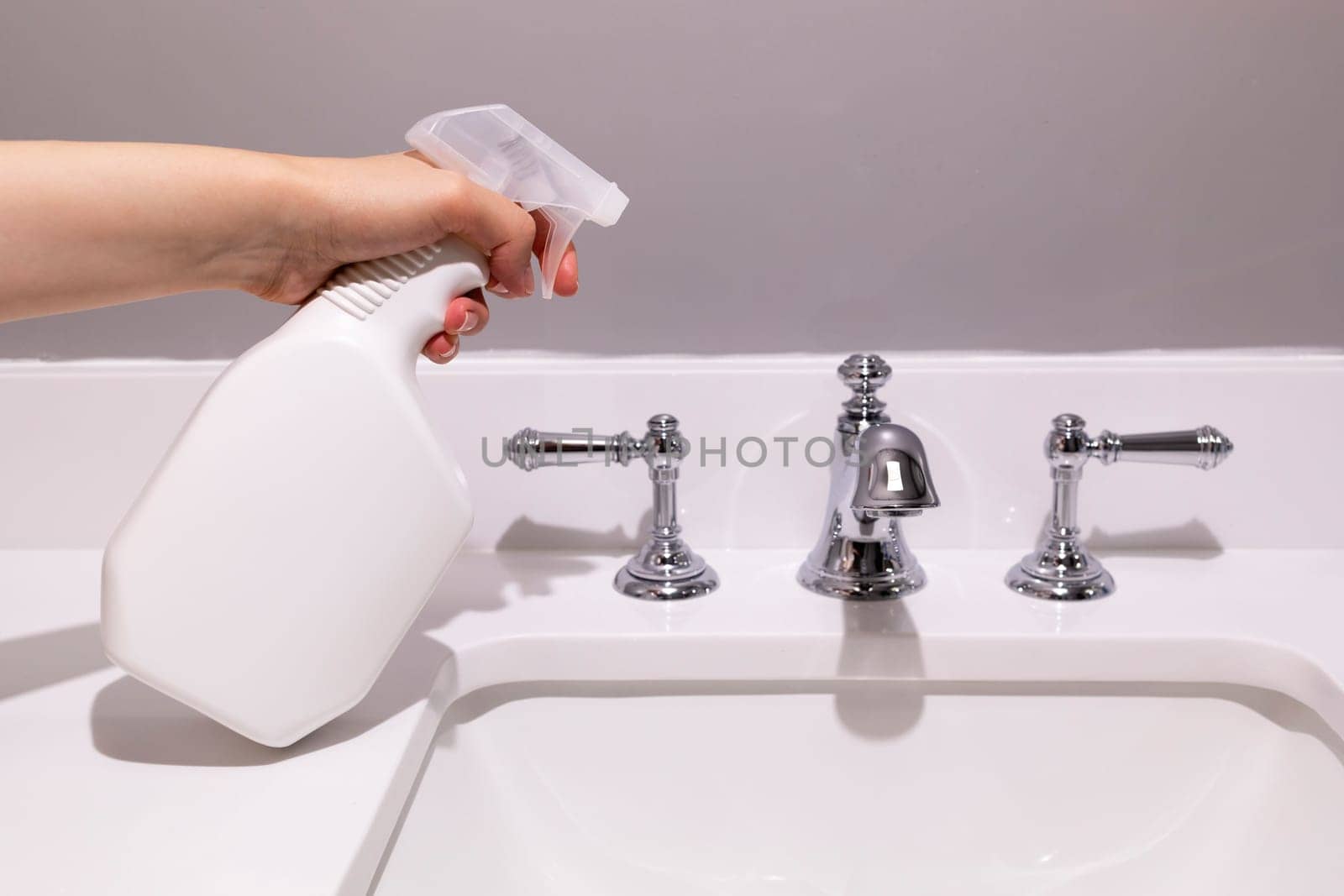 White Blank Plastic Spray Bottle In Female Hands On White Sink In Bathroom. Packaging Mockup. Blank Spray Bottle for Cleaning, Sanitary. Lifestyle. Empty Place For Text Or Logo Horizontal Plane