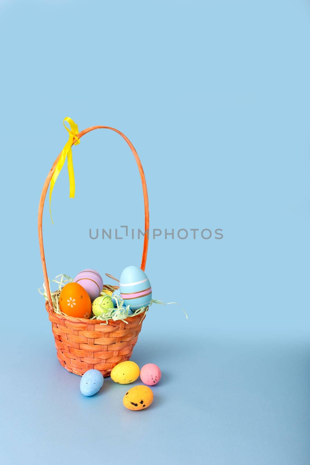 Easter basket filled with decorative multi colored eggs on a light blue background.Vertical