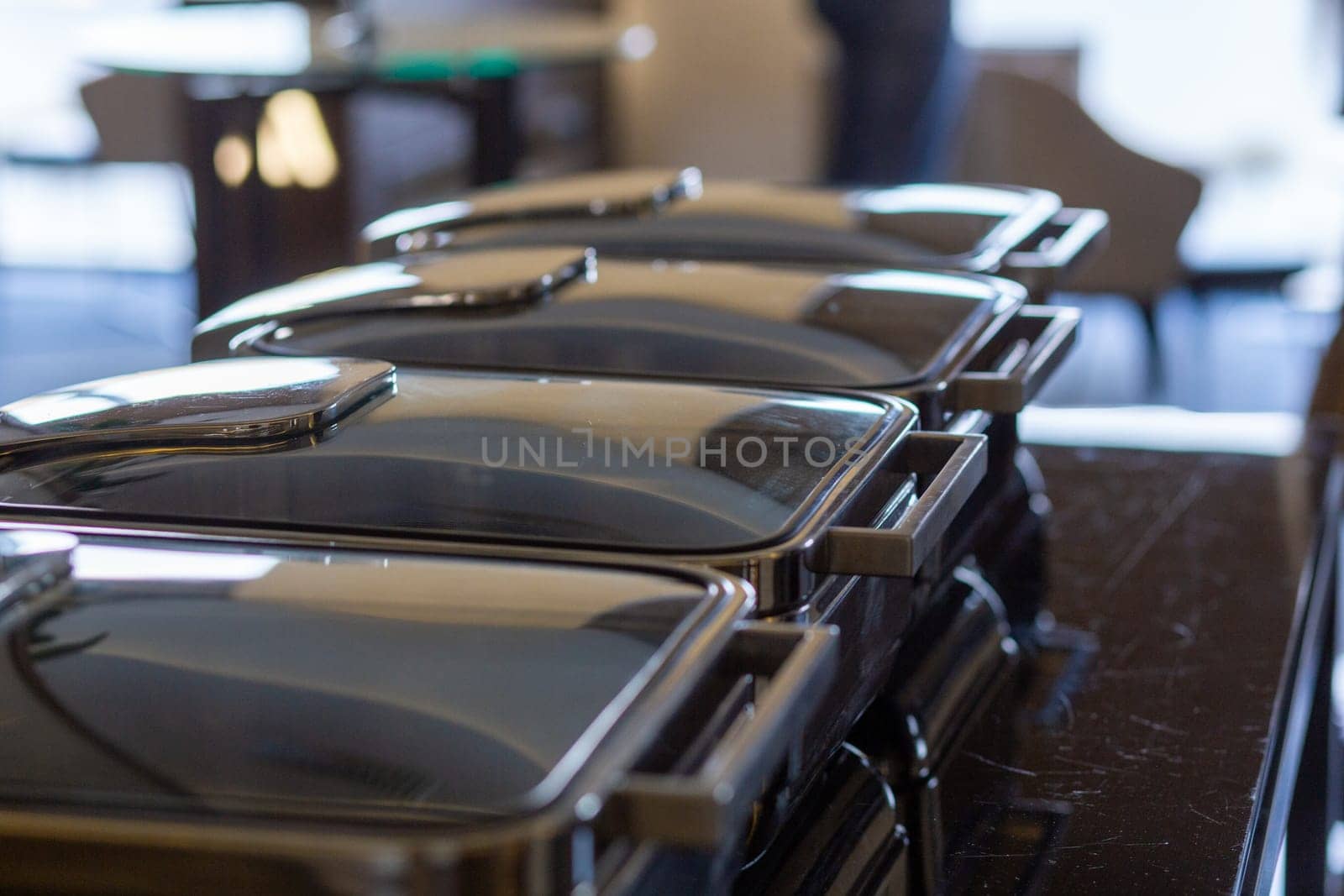 Row of closed buffet food dishes at party banquet hall. Chafing Dish ready for service made of stainless steel at buffet.