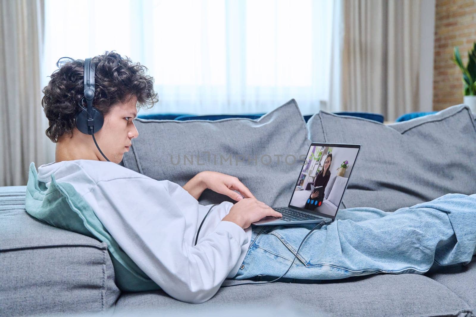 Online meeting with psychologist, young man lying on couch using video conference on laptop by VH-studio