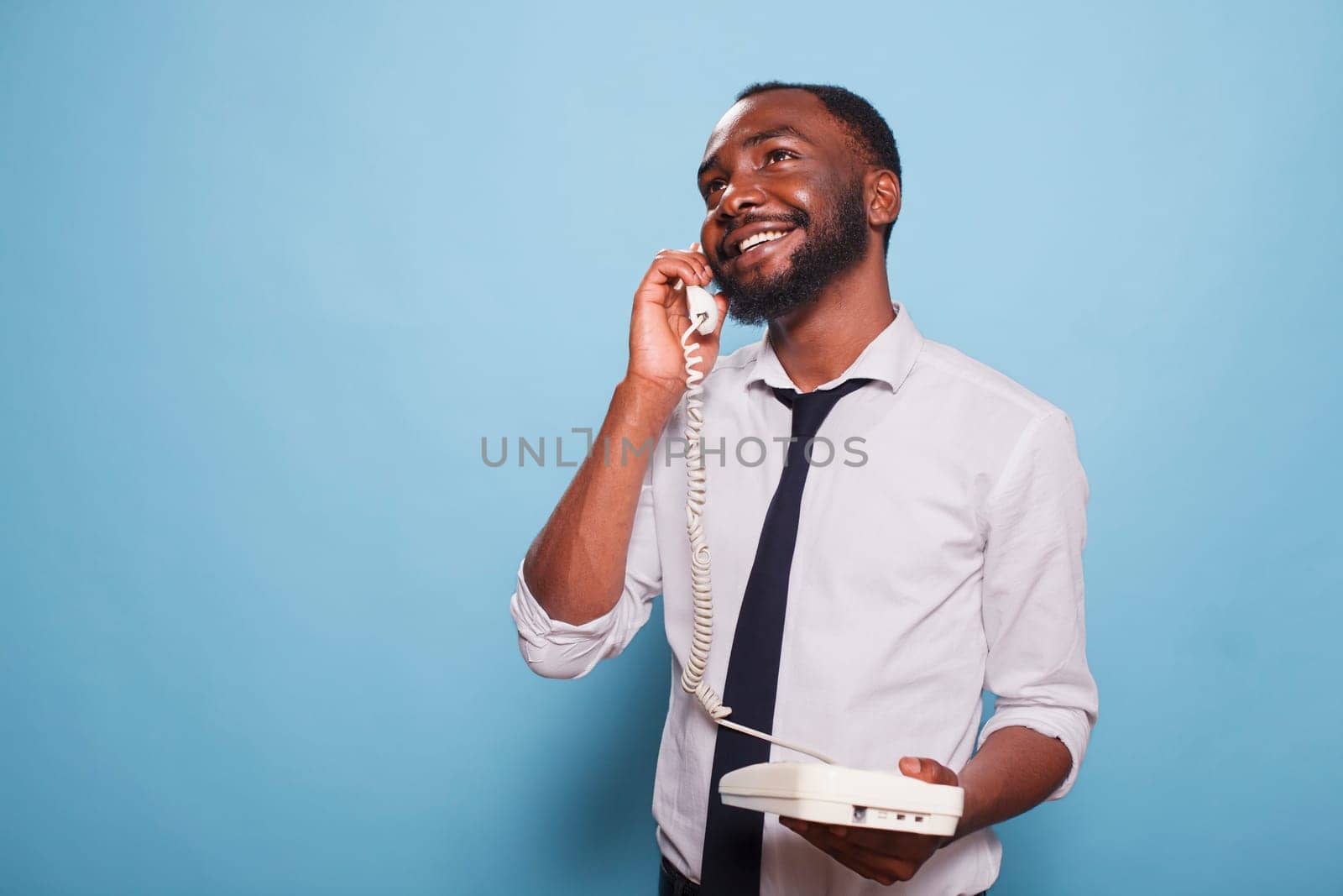 African american male adult making a phone call on a landline. Smiling businessman on an analogue telephone phone, chatting away. A contemporary individual having fun and taking calls