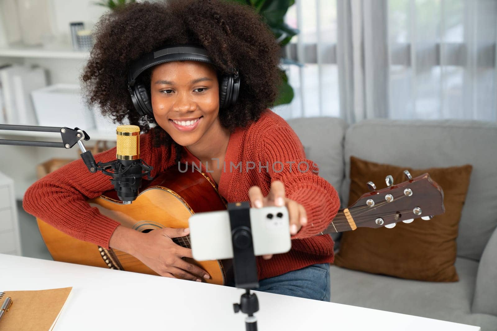 Host channel in musician of young African American playing guitar along with singing, broadcasting on smartphone in studio. Decoration of equipment headsets and recording microphone. Tastemaker.