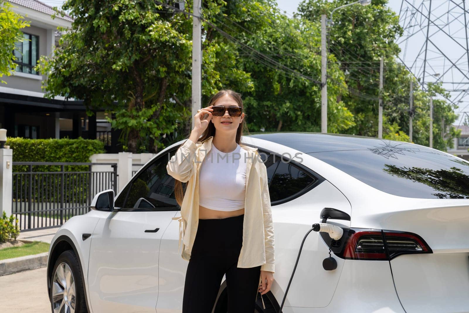 Eco-friendly conscious woman recharging EV vehicle from home charging station. EV electric car technology utilized as alternative transportation for future sustainability. Expedient