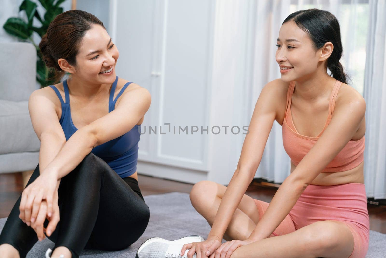 Asian woman in sportswear with her trainer or workout buddy, smiling and posing cheerful gesture. Home workout training or exercise fitness lifestyle in pursuit of healthy lifestyle. Vigorous