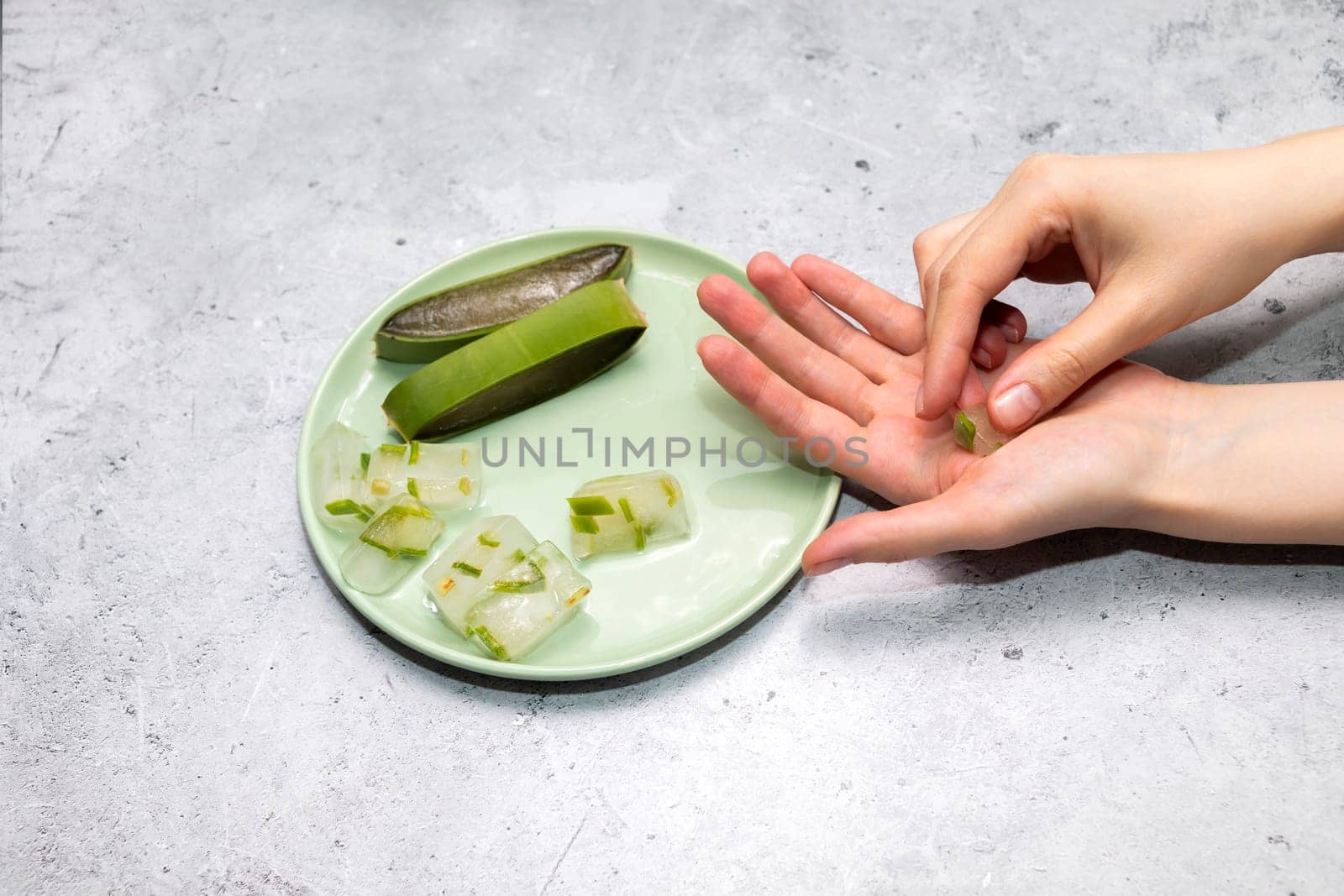 Top View Woman's Hand Holding Aloe Juice Ice Cubes, Aloe Vera Plant On Green Plate On Table. Flat Lay Horizontal plane. Natural Homemade Cosmetics, DIY Concept. Food, Medicine And Beauty Industry by netatsi