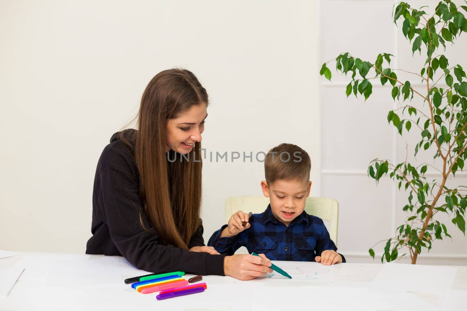 Mom and son learn to draw pictures at home at the table by Simakov