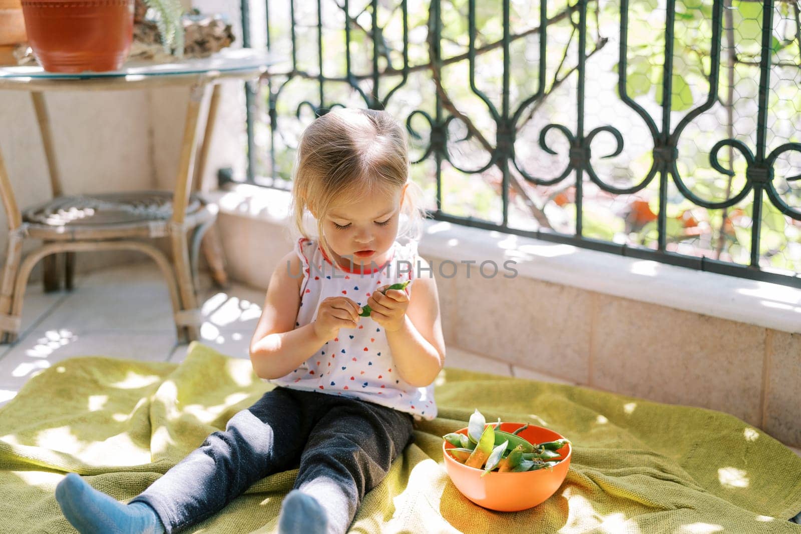 Little girl sitting on a blanket and peeling green beans. High quality photo