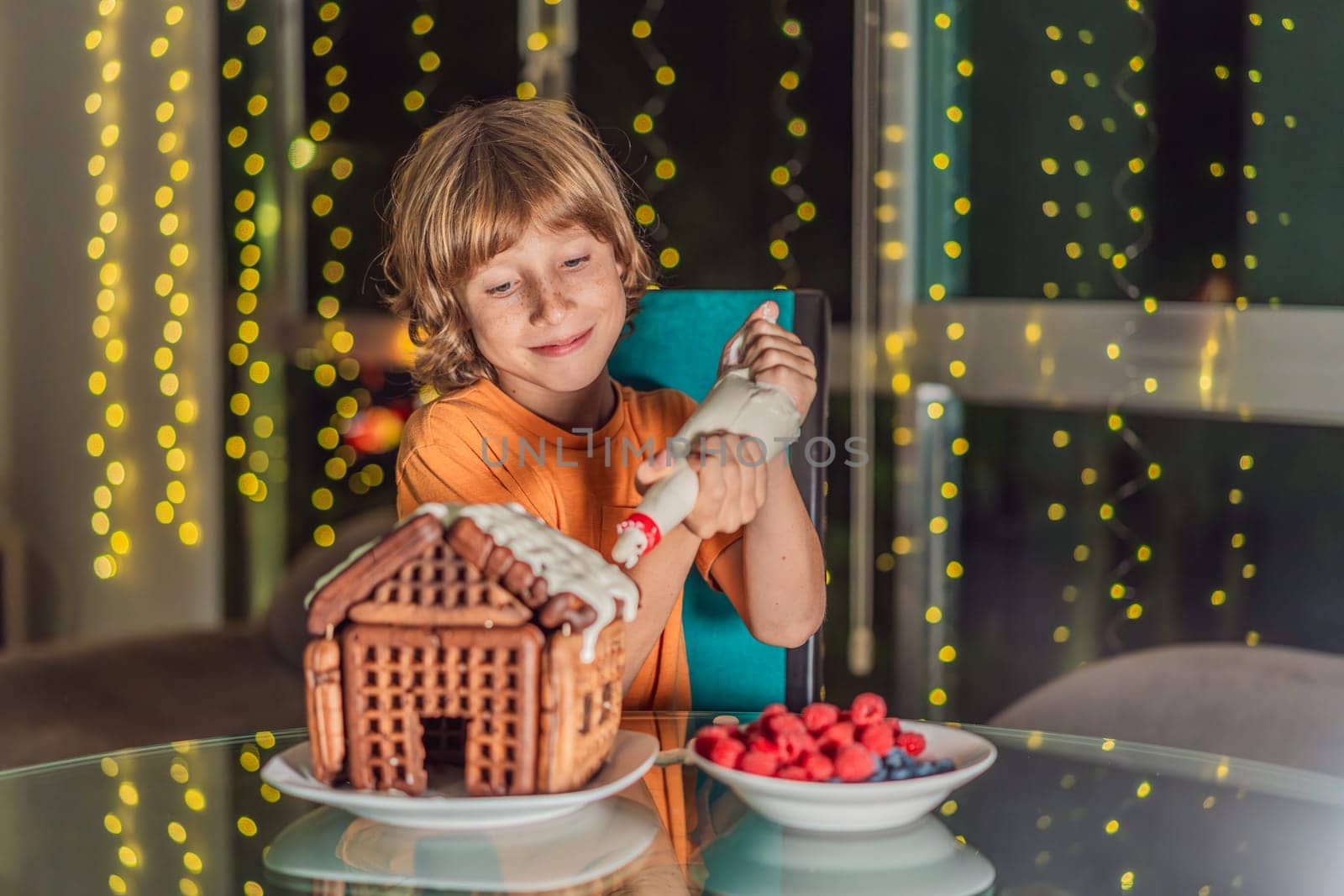 Immerse in festive delight as a boy crafts boy crafting an unconventional gingerbread house, infusing Christmas with unique creativity and festive cheer. A sweet scene of seasonal bonding and culinary fun by galitskaya