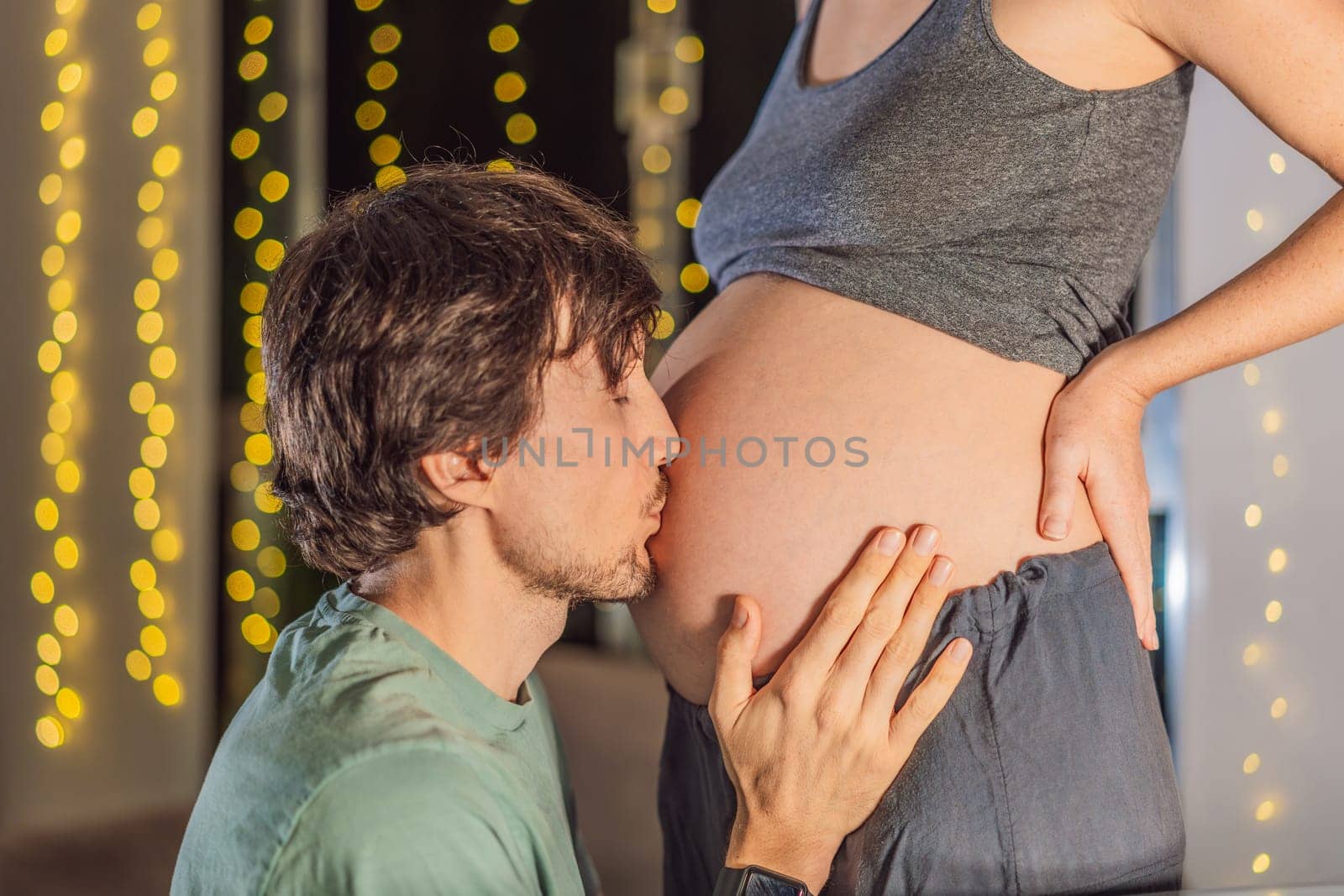 In a tender holiday moment, a husband kisses his wife's pregnant belly, expressing love and anticipation for the Christmas joy to come by galitskaya