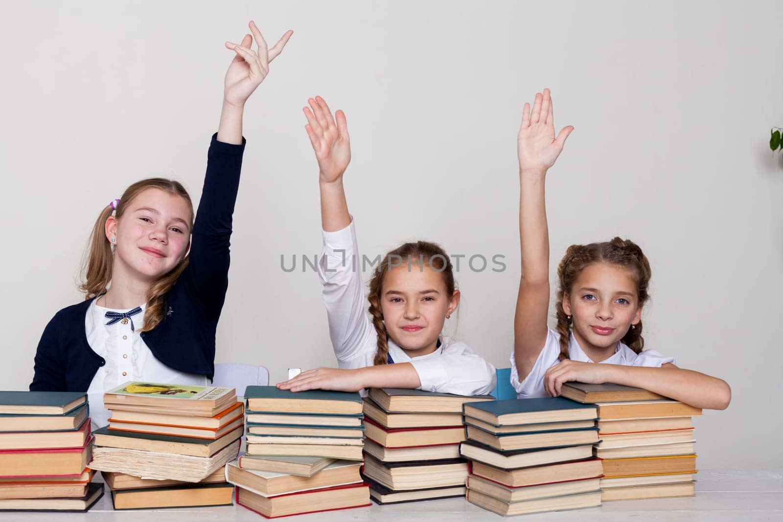 thre girls with books in class at a desk at school by Simakov
