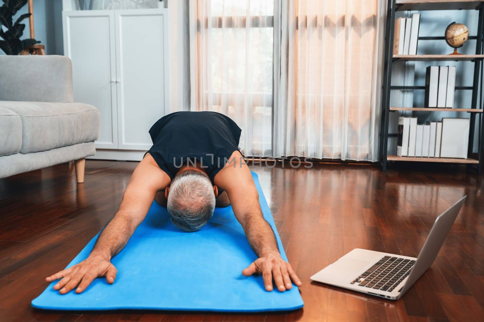 Senior man in sportswear being doing yoga in meditation posture on exercising mat at home. Healthy senior pensioner lifestyle with peaceful mind and serenity. Clout