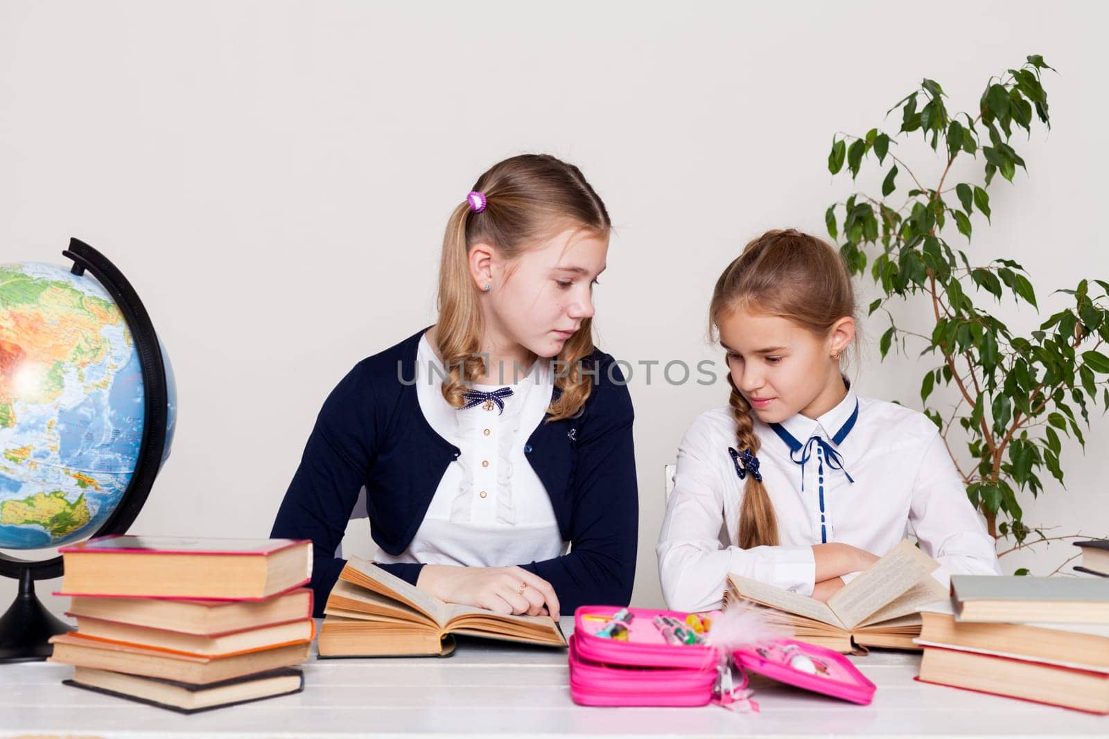 two girls with books and a globe in class at the desk at school by Simakov