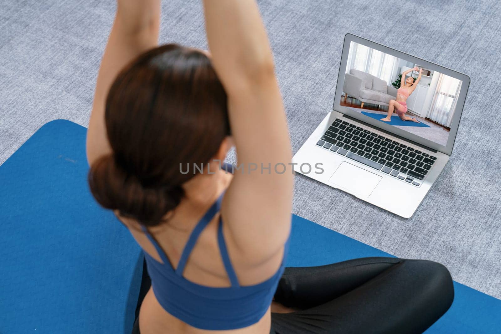 Asian woman in sportswear doing yoga exercise on fitness mat as her home workout training routine. Healthy body care lifestyle woman watching online yoga video on laptop. Vigorous