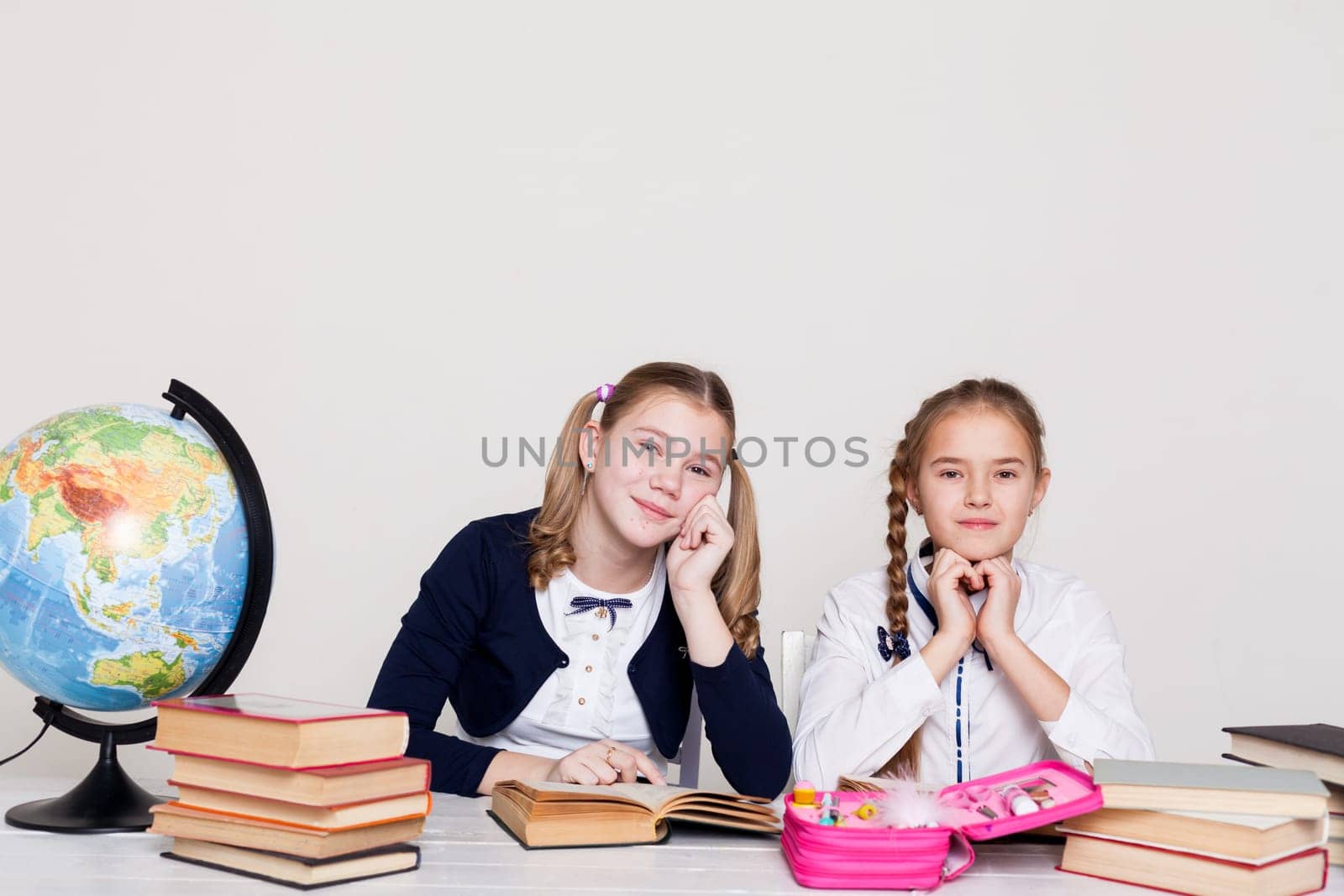 two girls with books and a globe in class at the desk at school by Simakov