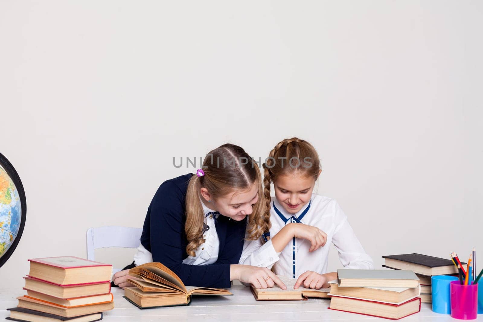 two girls with books and a globe in class at the desk at school by Simakov