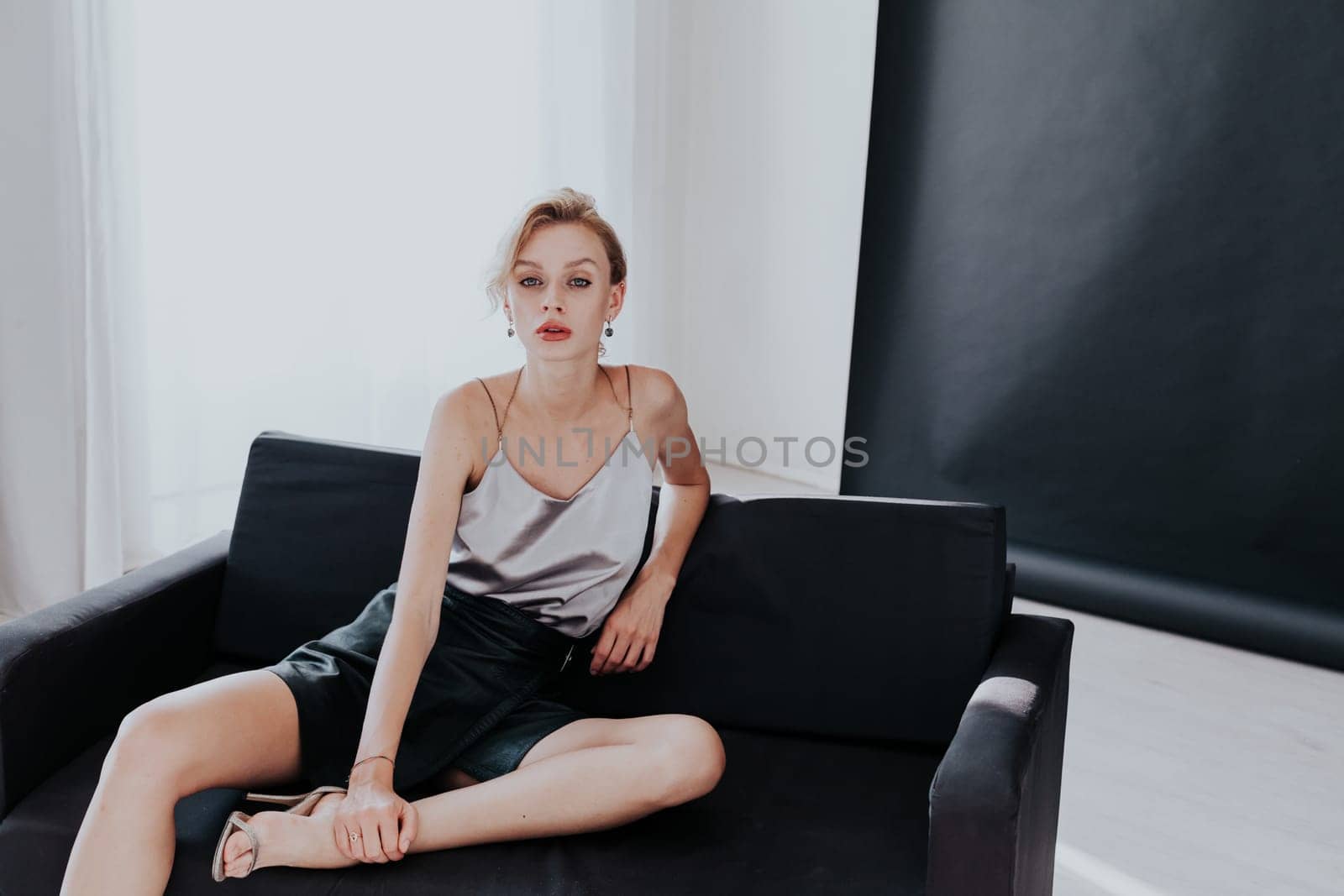 Portrait of a beautiful fashionable woman sits on a black office sofa by Simakov