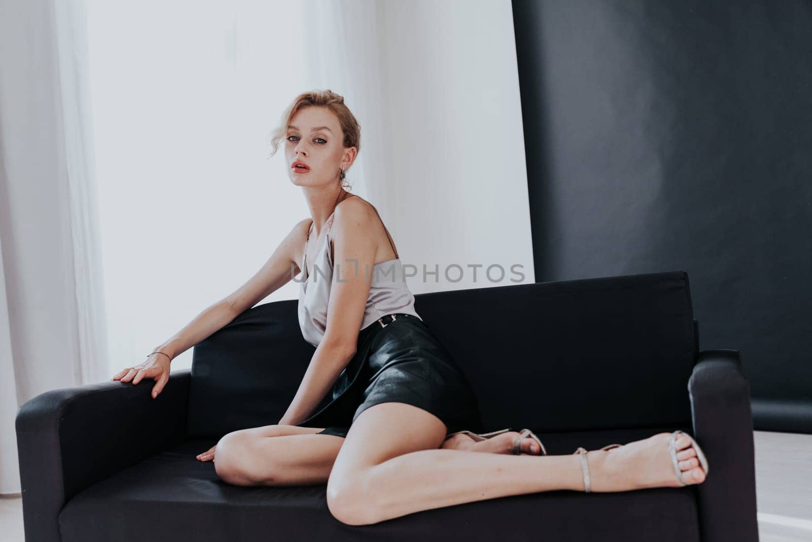 Portrait of a beautiful fashionable woman sits on a black office sofa by Simakov