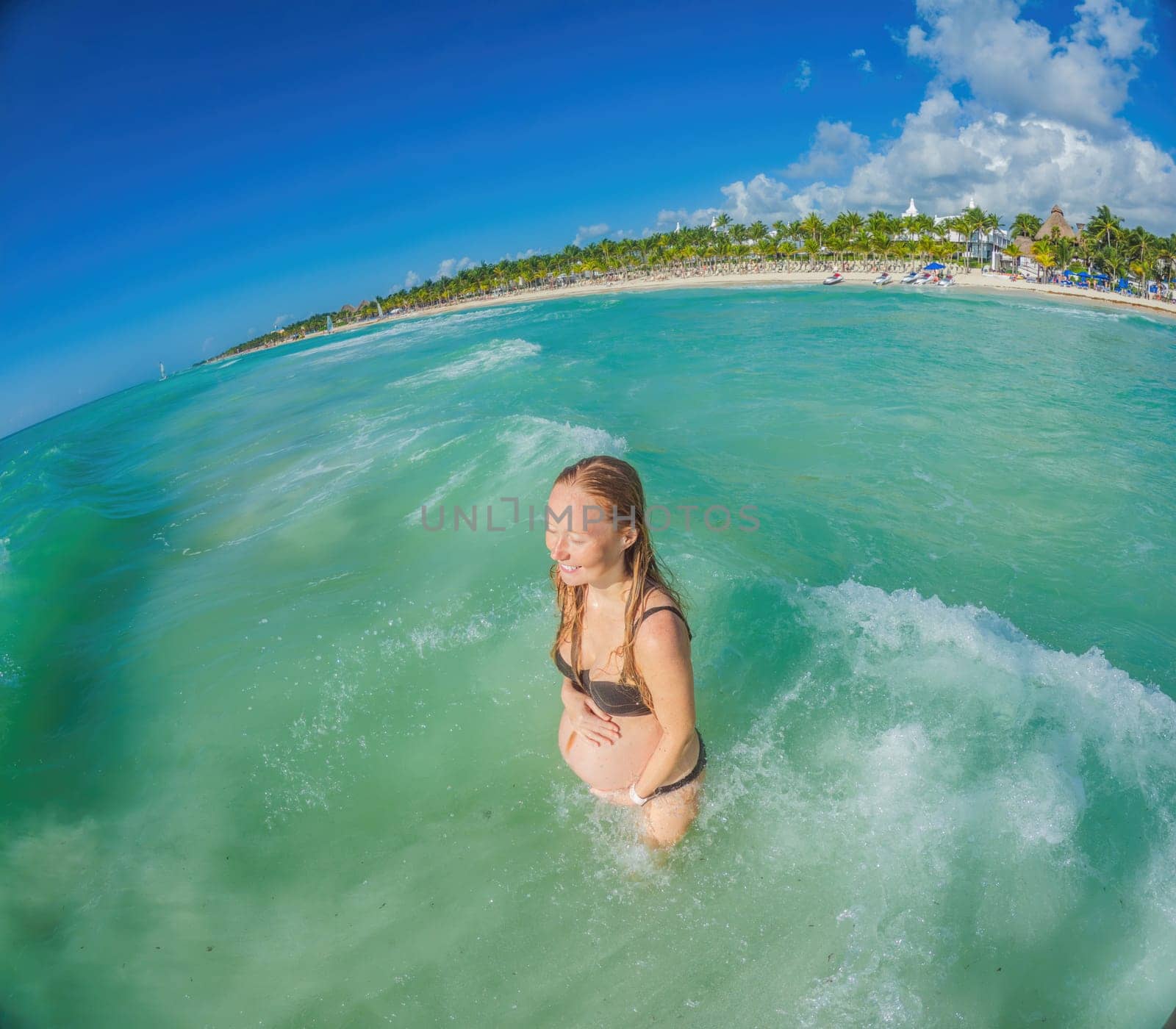 A radiant pregnant woman revels in the serenity of the turquoise sea, embracing the soothing waves as she celebrates the beauty of impending motherhood.