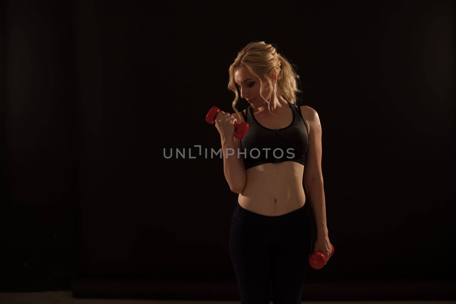 Blonde woman sports in the gym with fitness dumbbells by Simakov