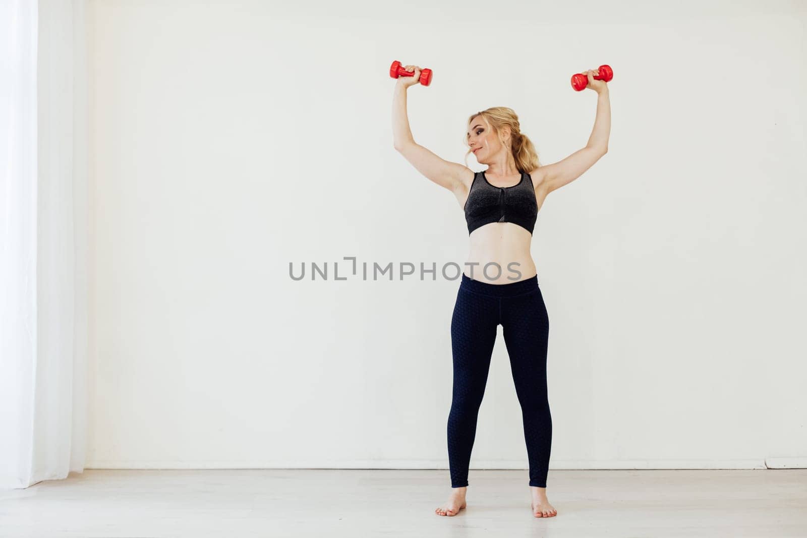 Blonde woman sports in the gym with fitness dumbbells by Simakov