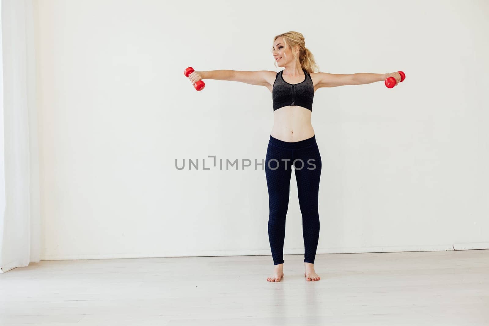 Blonde woman sports in the gym with fitness dumbbells by Simakov