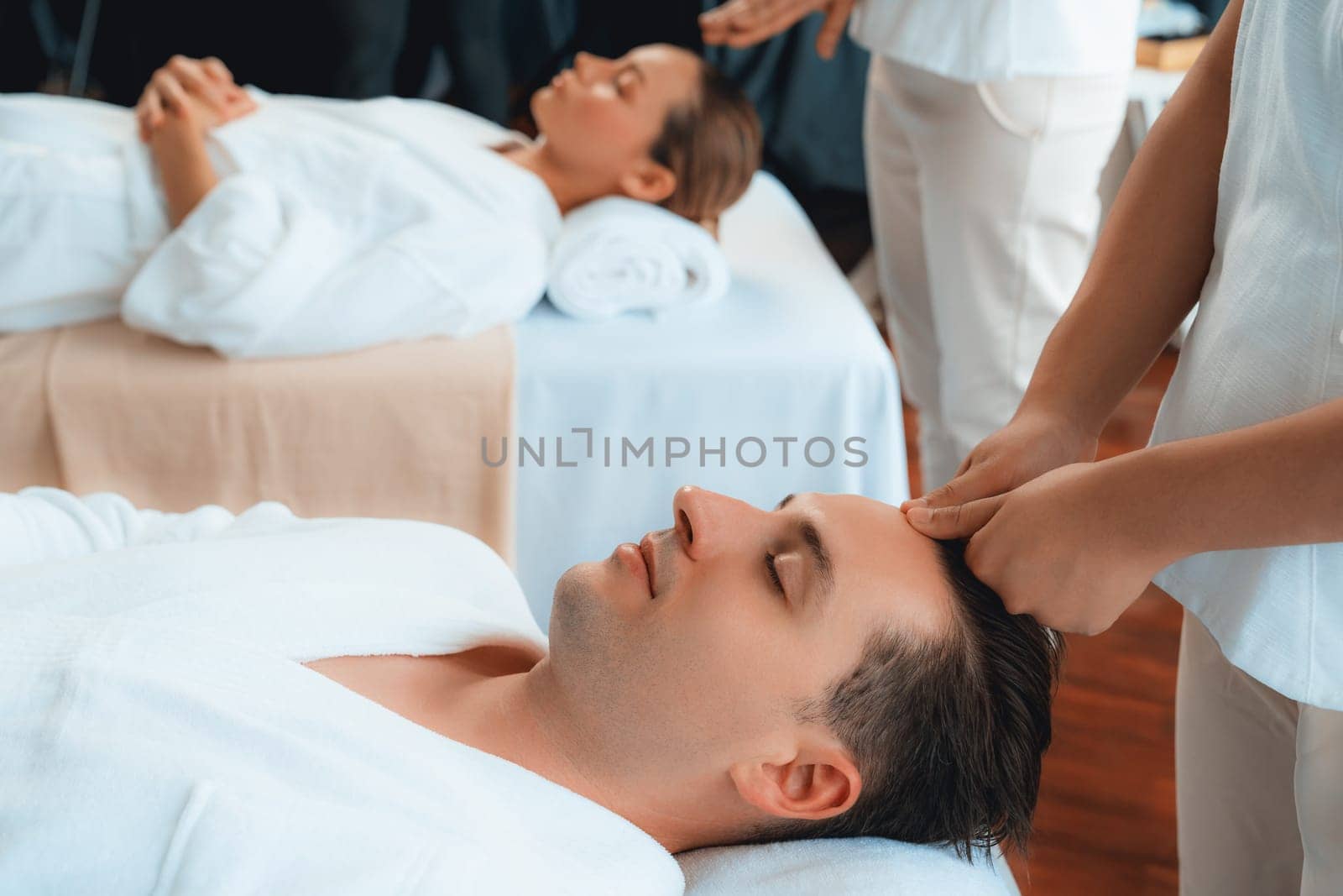 Caucasian couple enjoying relaxing anti-stress head massage and pampering facial beauty skin recreation leisure in dayspa modern light ambient at luxury resort or hotel spa salon. Quiescent