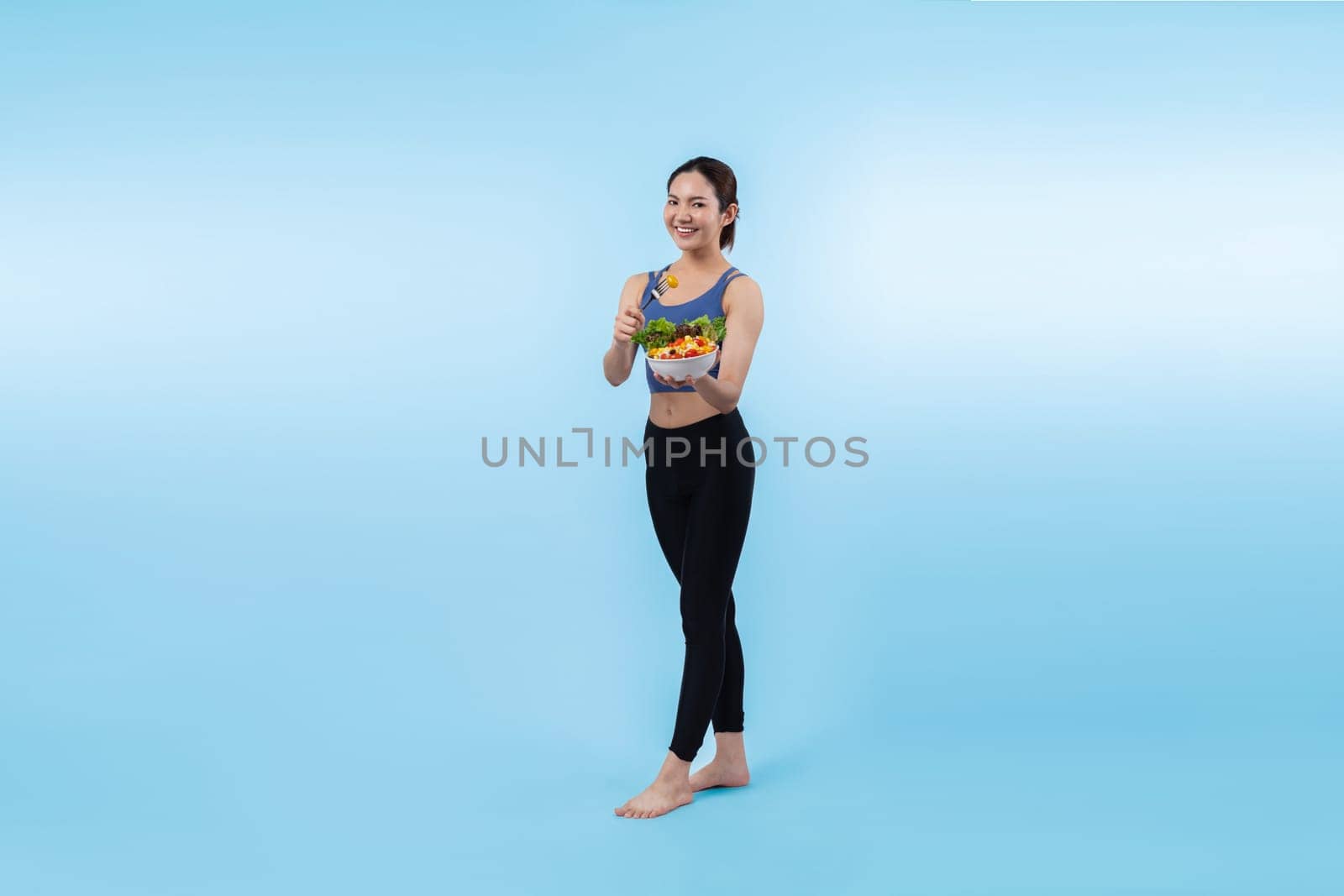 Young sporty Asian woman in sportswear holding salad bowl fill with vibrant of fruit and vegetable. Natural youthful and fit body lifestyle with balance nutrition on isolated background. Vigorous