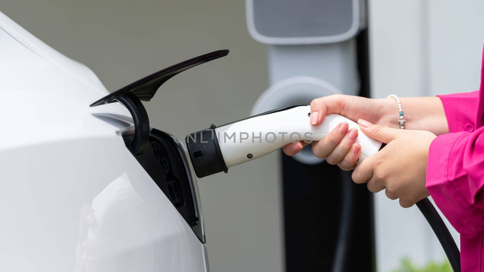 Modern eco-friendly woman recharging electric vehicle from home EV charging station. EV car technology utilized for home resident to future environmental sustainability. Panorama Synchronos