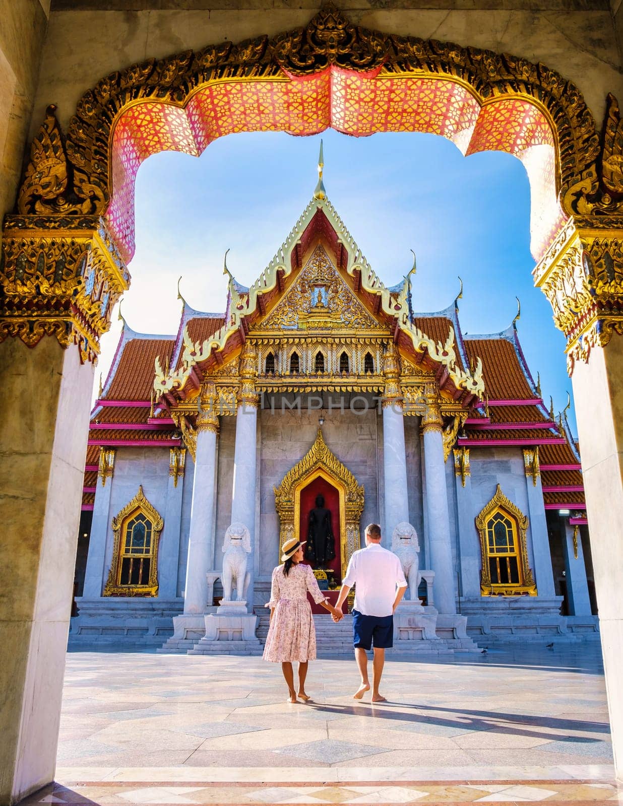 Wat Benchamabophit temple in Bangkok Thailand, The Marble temple in Bangkok. Asian woman with a hat and European men visiting a temple, a couple on a city trip in Bangkok during summer