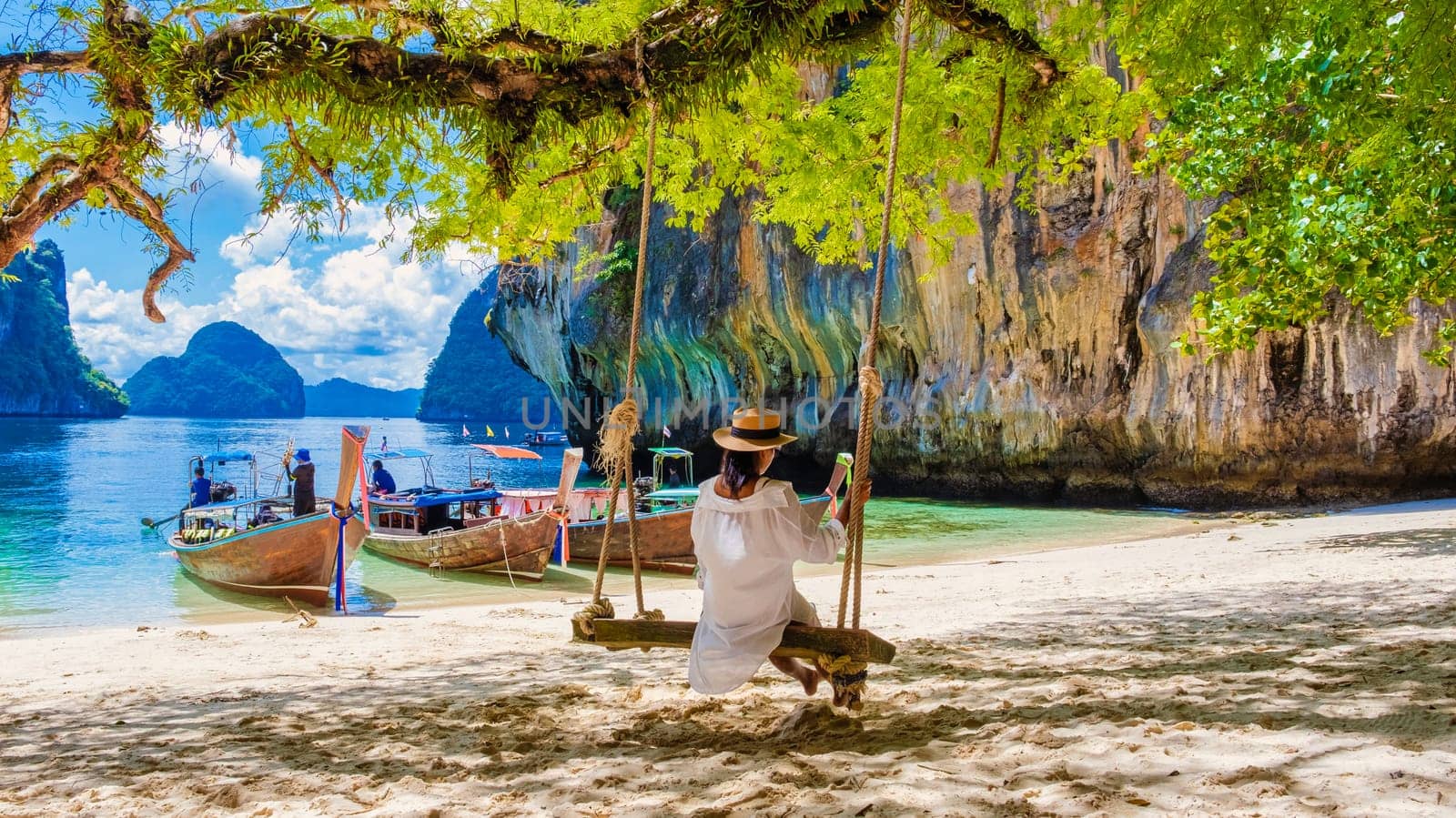 women on a swing at the Tropical lagoon of Koh Loa Lading Krabi Thailand part of the Koh Hong Islands in Thailand. beautiful beach with limestone cliffs and longtail boats on a sunny day