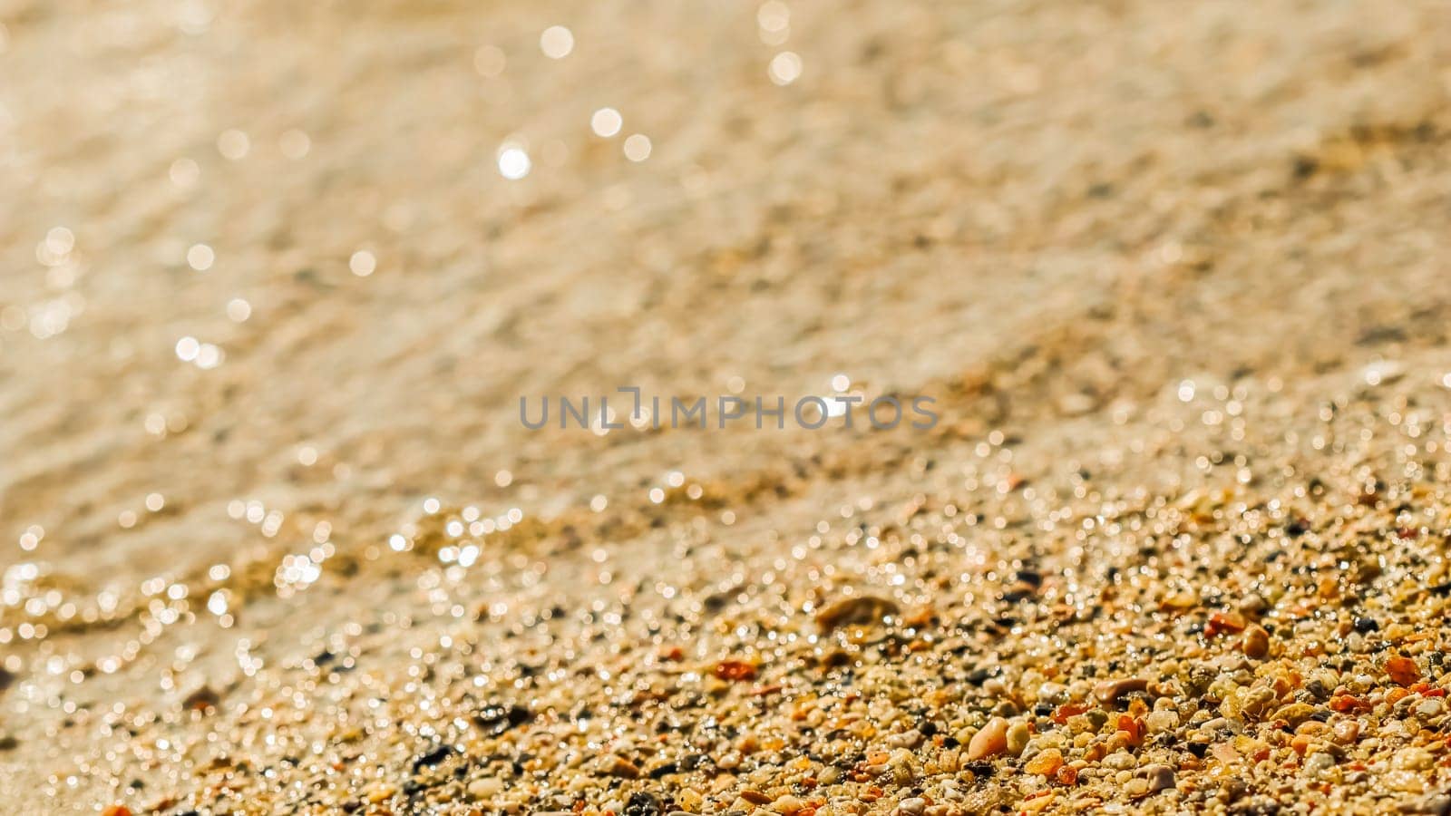 A background of sand, small pebbles and flowing waves on the sea beach. Summer vacation concept by Olayola