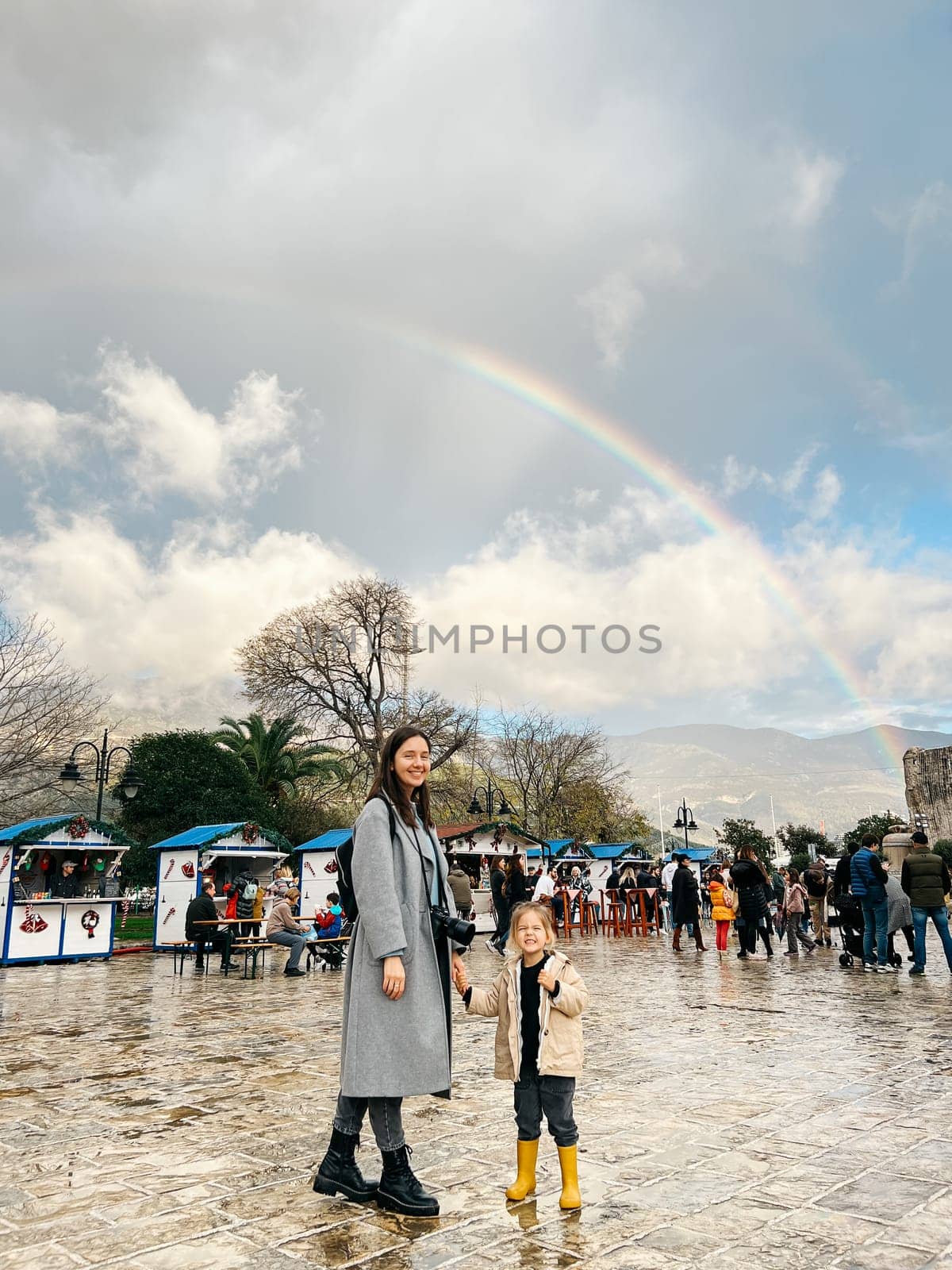 Mom with a little girl are standing near the market against the backdrop of a rainbow over the mountains. High quality photo
