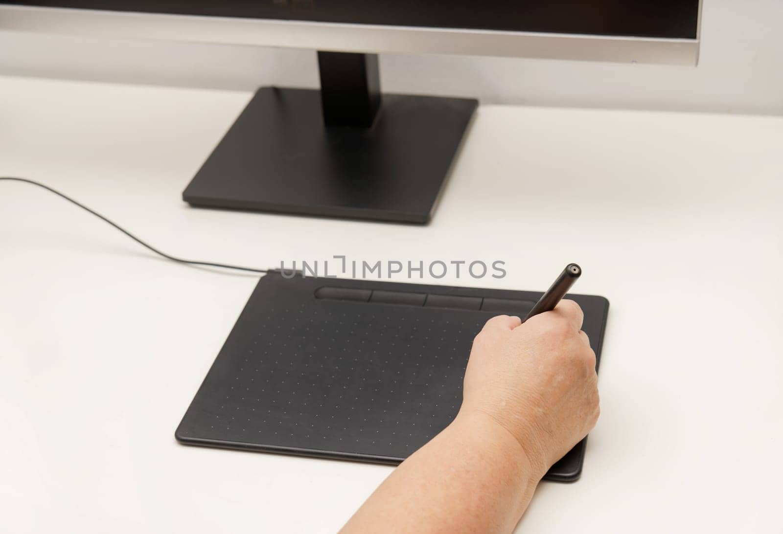 Woman hand working on her computer with a digital graphic tablet, in the background a monitor with an image